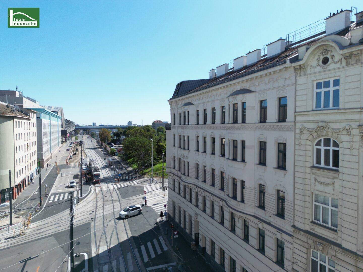 Blick auf die belebte Stadtstraße mit Straßenbahnschienen und die Seitenfassade des Gebäudes.