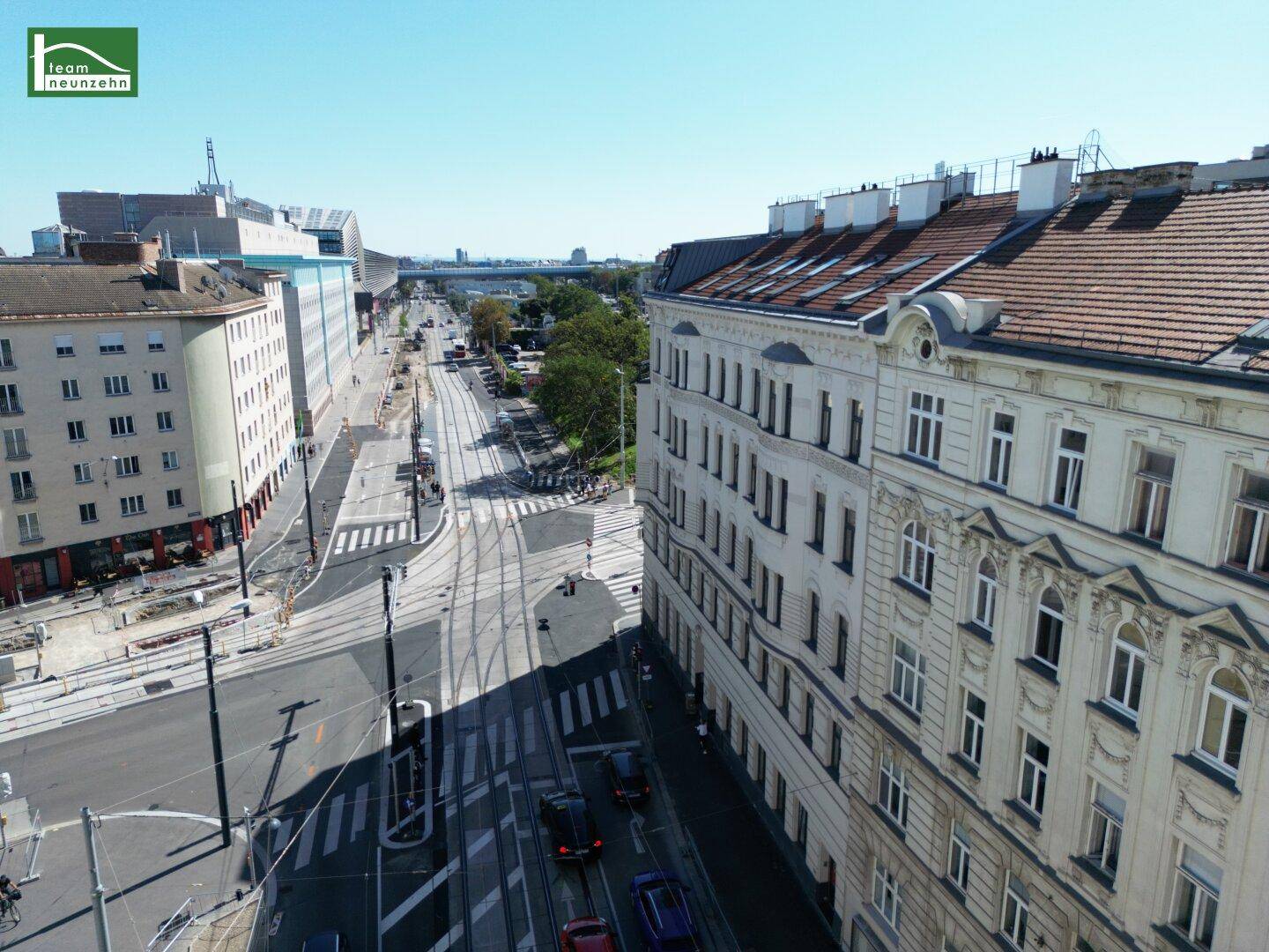 Luftaufnahme einer belebten Stadtstraße mit dem weißen Gebäude auf der rechten Seite und weiteren Gebäuden im Hintergrund.