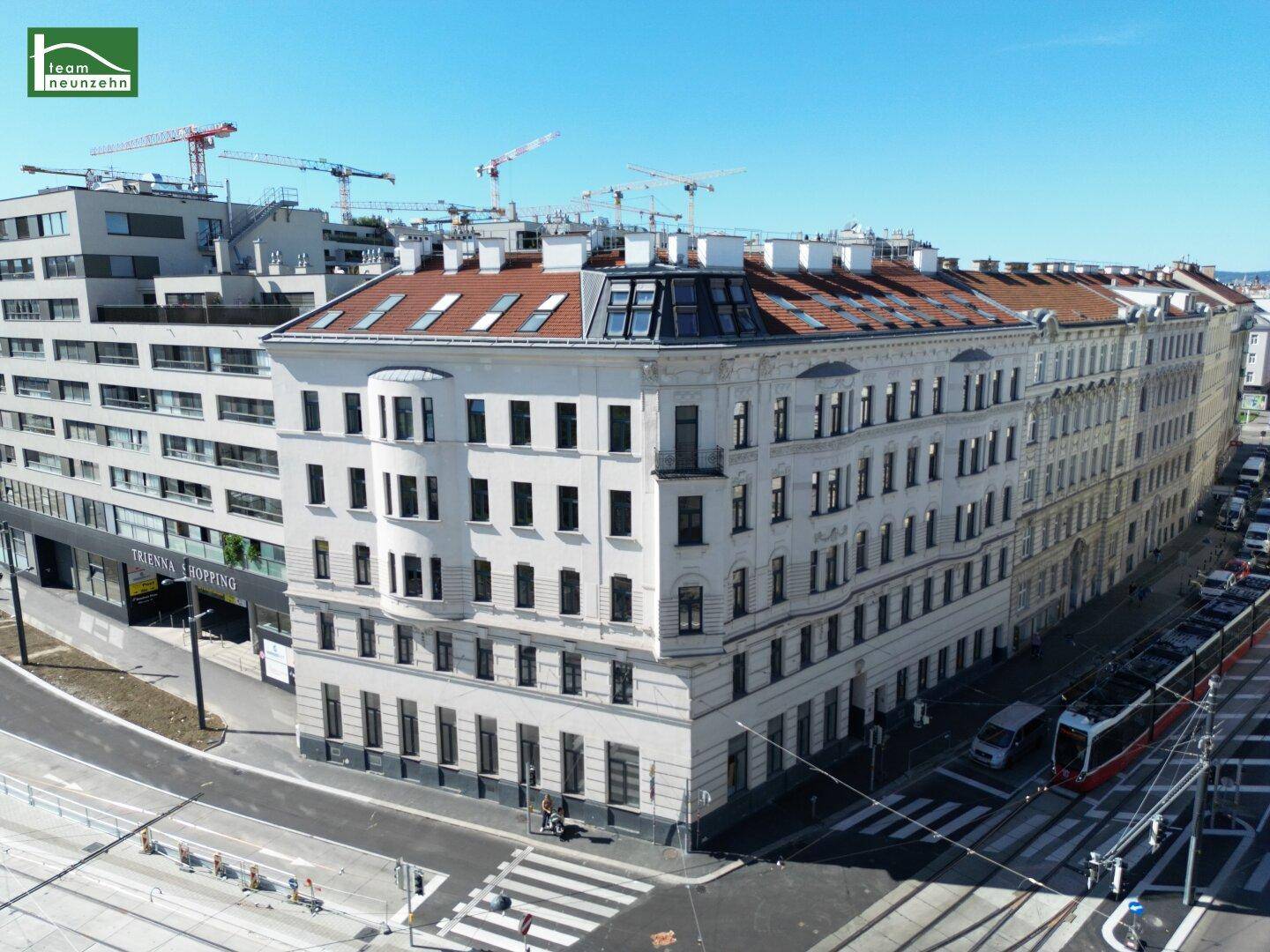 Panoramablick auf ein Eckgebäude mit Mansarddach in einer belebten Stadtlandschaft.