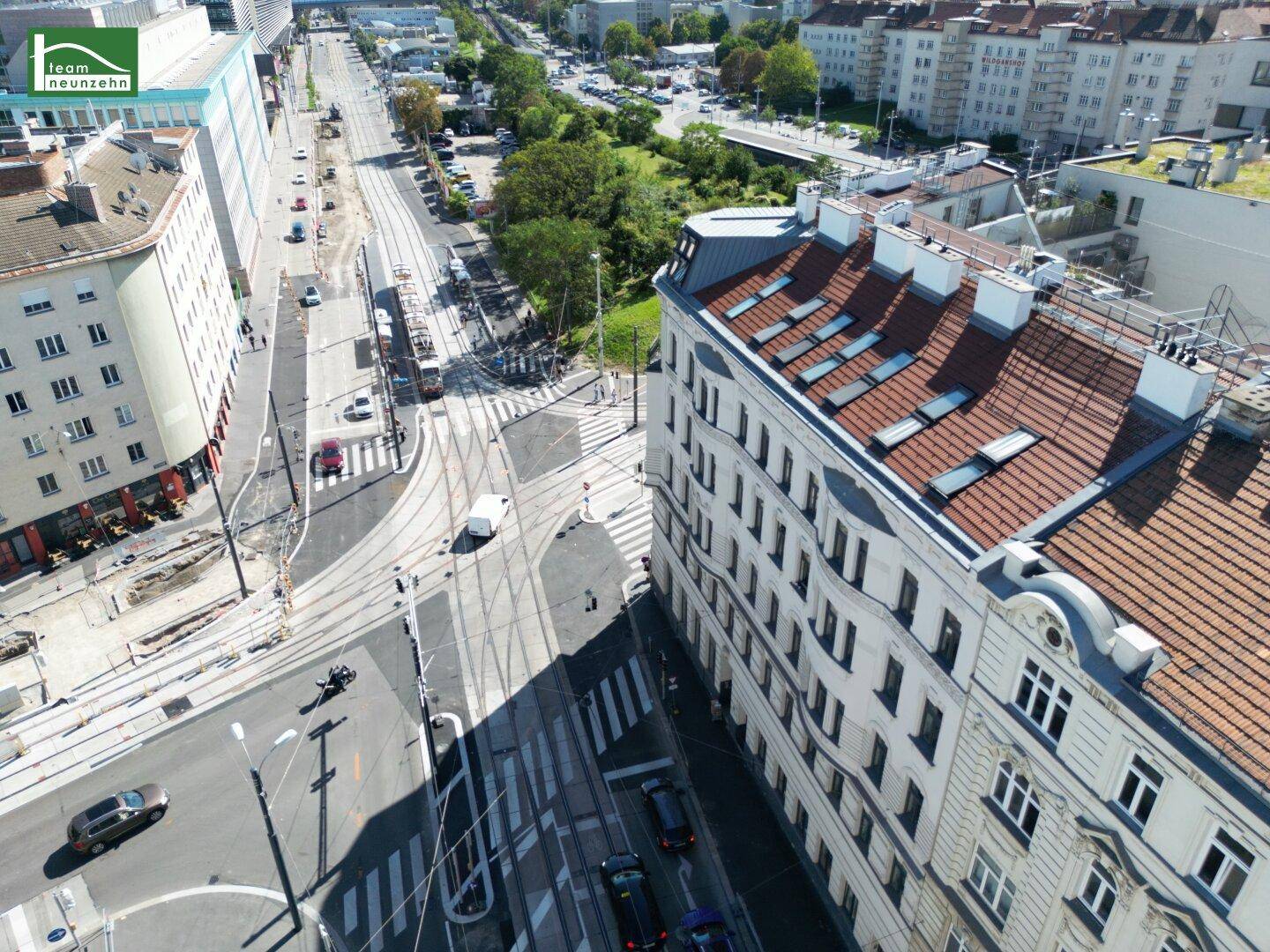 Luftaufnahme einer belebten Stadtkreuzung mit historischen Gebäuden und Straßenbahnen.