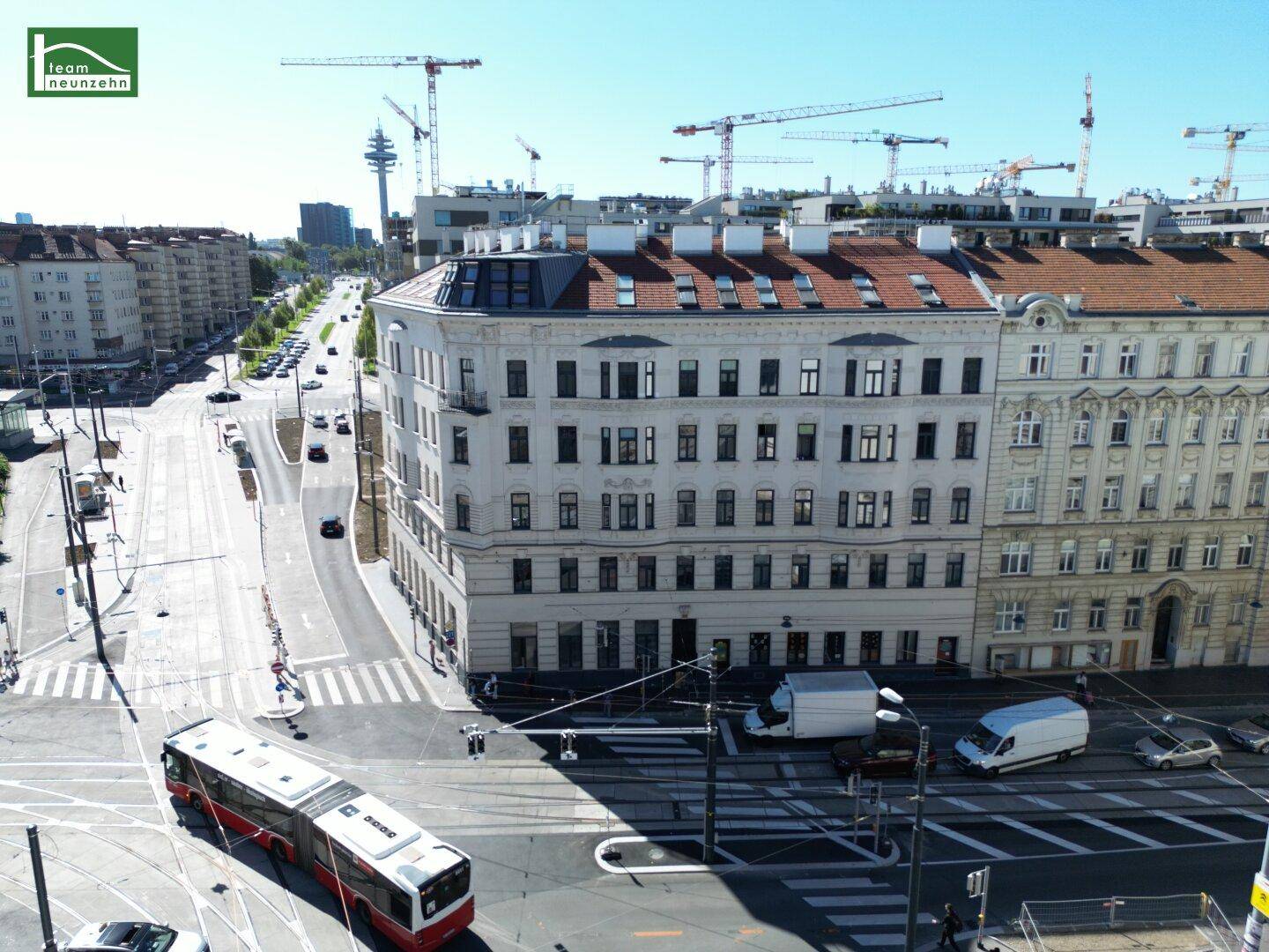 Luftaufnahme einer belebten Stadtkreuzung mit historischen Gebäuden und modernen Baukränen im Hintergrund.
