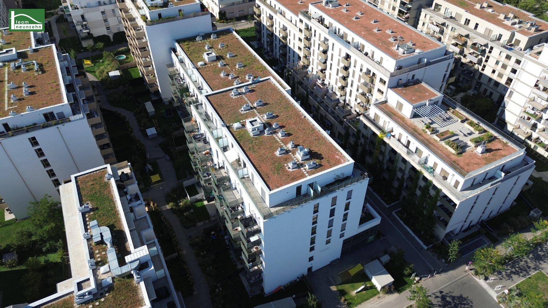 Vogelperspektive eines modernen Wohnkomplexes mit begrünten Dächern und Balkonen in einer städtischen Umgebung.