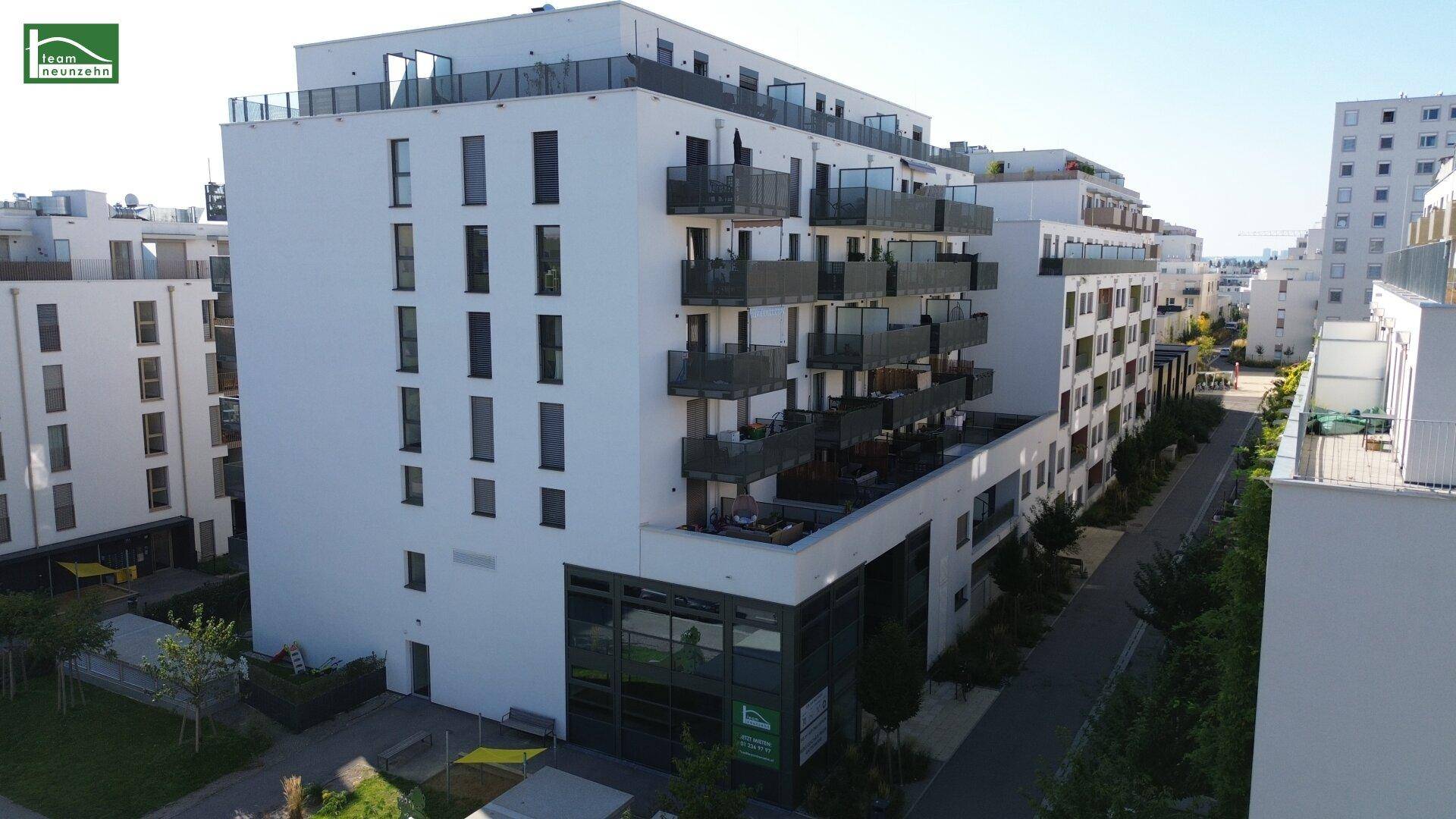 Luftaufnahme eines modernen Wohngebäudes mit weißer Fassade und zahlreichen Balkonen in einer städtischen Umgebung.