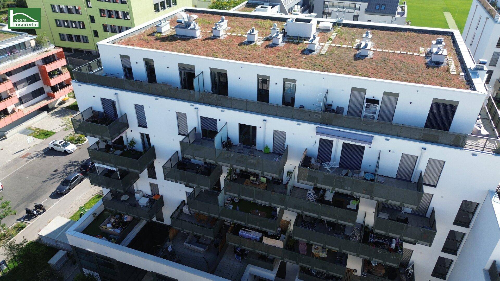 Nahaufnahme der modernen Fassade eines Apartmentgebäudes mit begrüntem Flachdach und möblierten Balkonen.