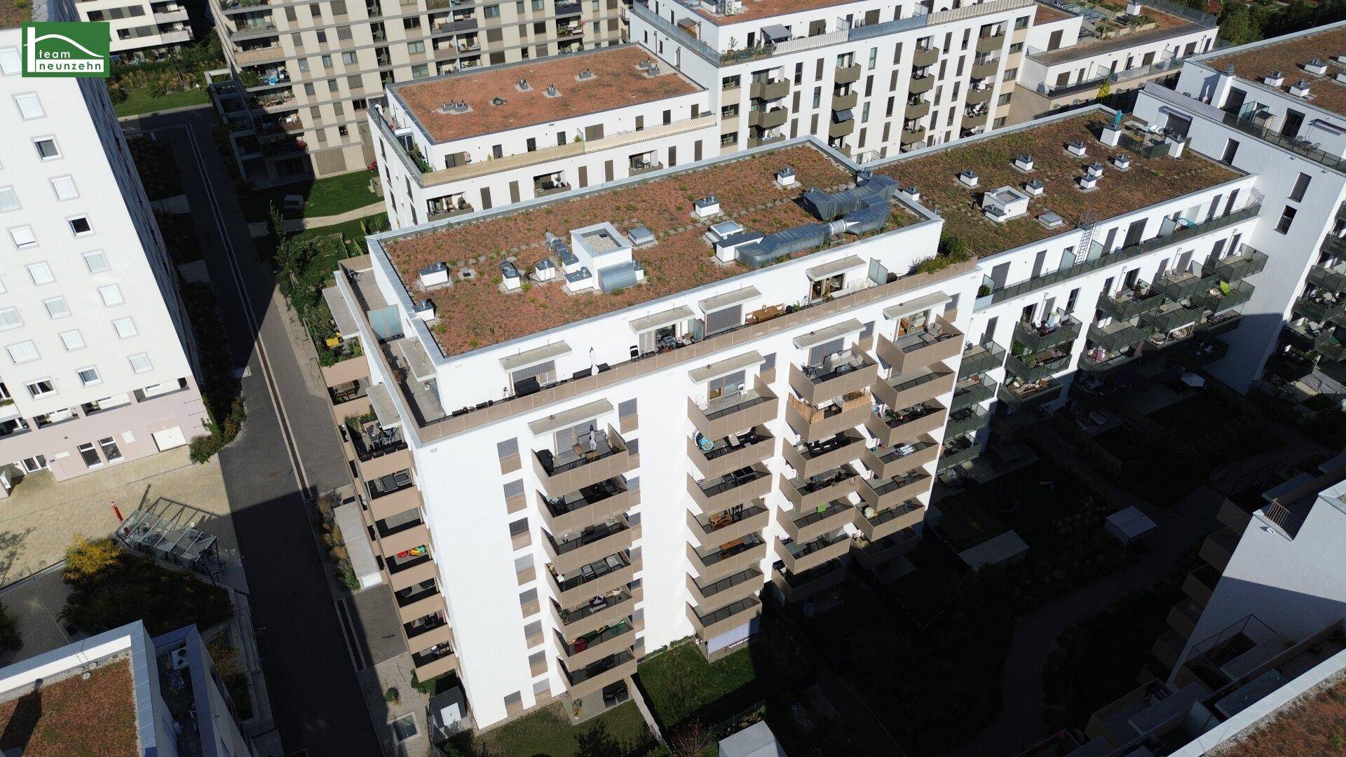 Luftaufnahme eines modernen Apartmentgebäudes mit begrünten Dächern und zahlreichen Balkonen in einer städtischen Umgebung.