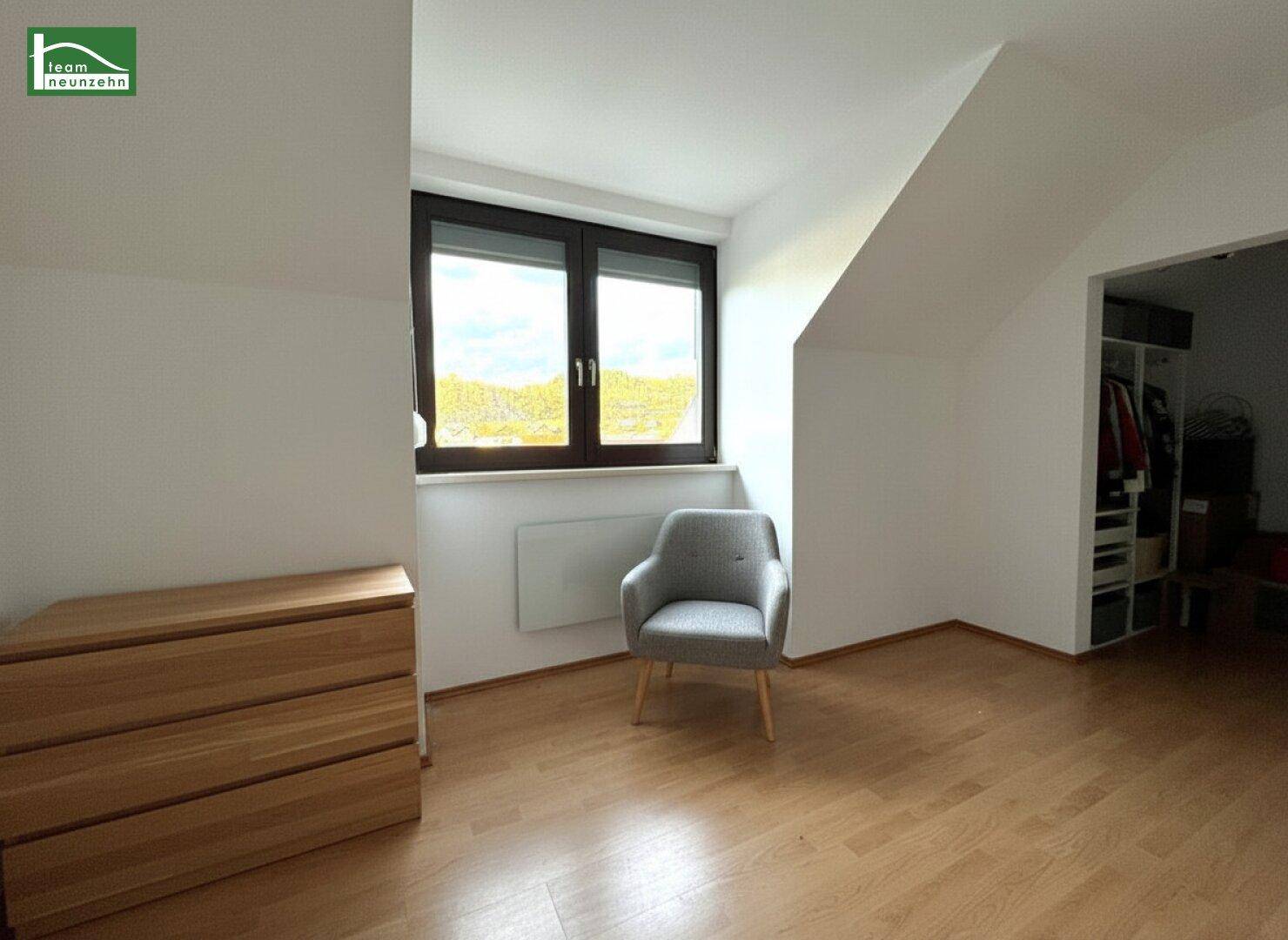 Schlafzimmer mit Holzboden, Kommode und Blick ins Grüne.