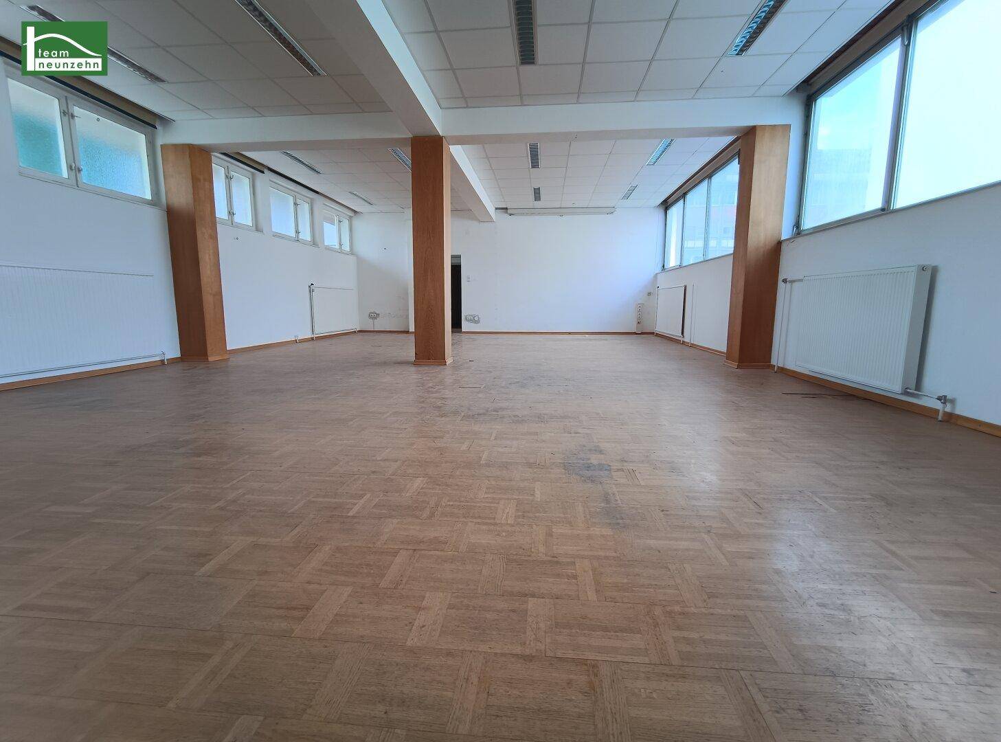 Geräumiger, leerer Gewerberaum mit Holzparkettboden und großen Fenstern, bereit zur individuellen Gestaltung und Nutzung.