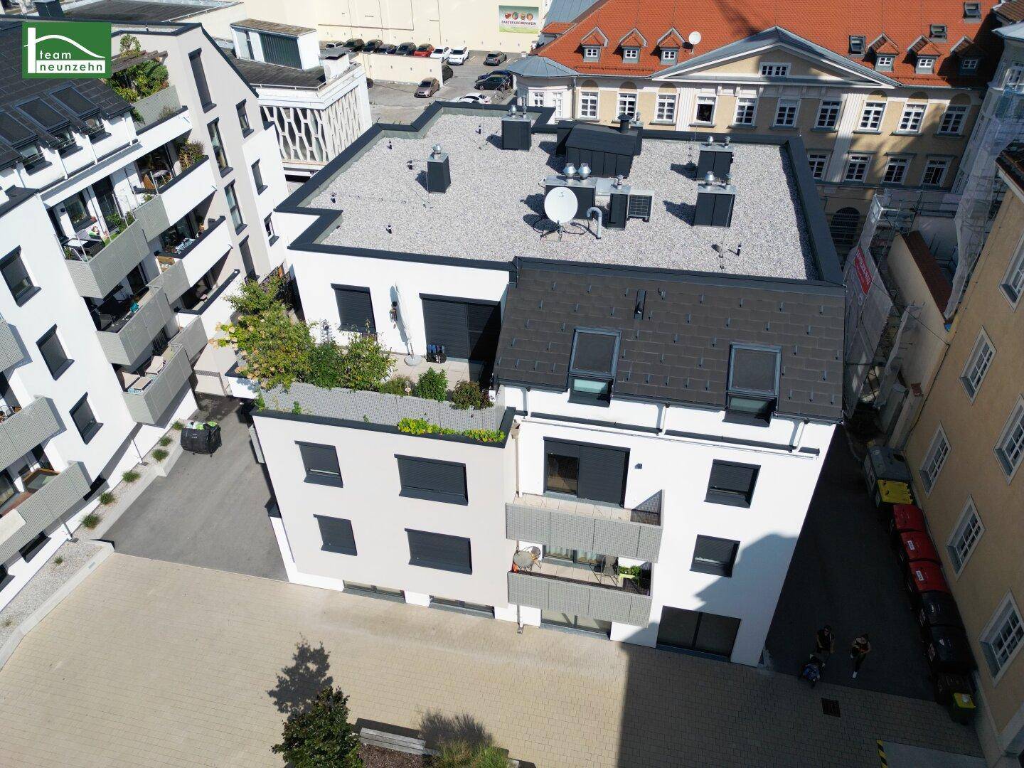 Luftaufnahme eines modernen Wohngebäudes mit Flachdach und begrünten Terrassen in städtischer Umgebung.
