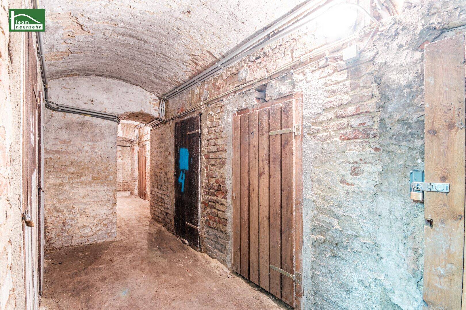 Rustikaler Kellergang mit unverputzten Ziegelwänden, einem Gewölbedecke und Holztüren zu den einzelnen Abteilen.