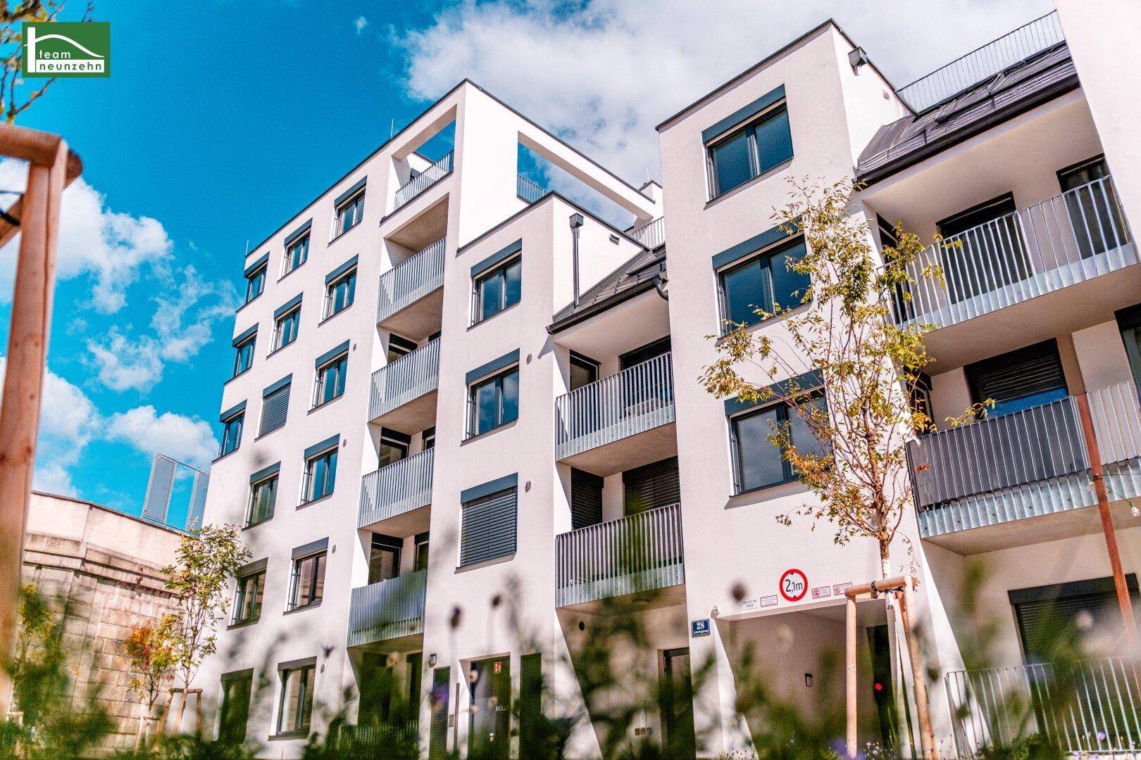 Modernes Mehrfamilienhaus mit weißer Fassade, Balkonen und großen Fenstern unter blauem Himmel.