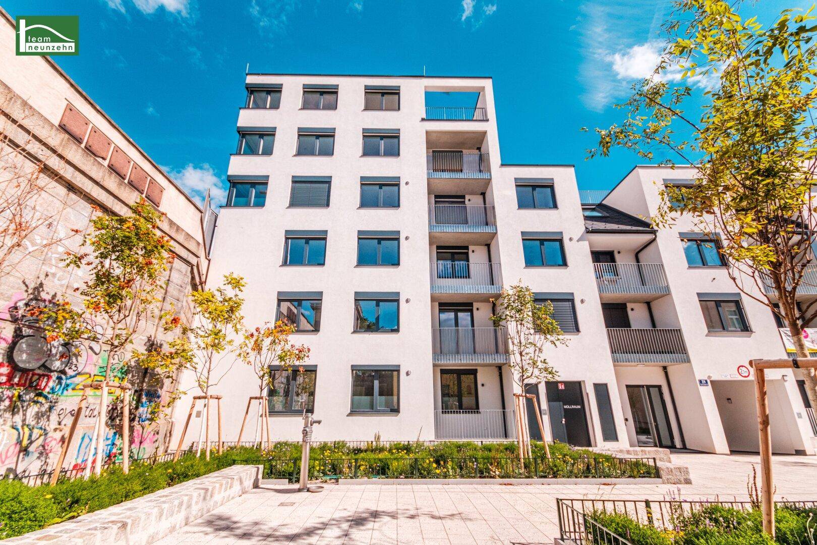Ansicht des modernen Wohngebäudes mit weißer Fassade und Balkonen, umgeben von urbaner Landschaft.