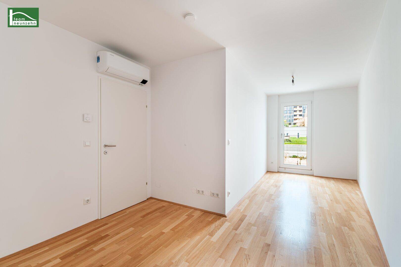 Helles Zimmer mit Holzboden, Klimaanlage und einem Fenster, das Tageslicht spendet.