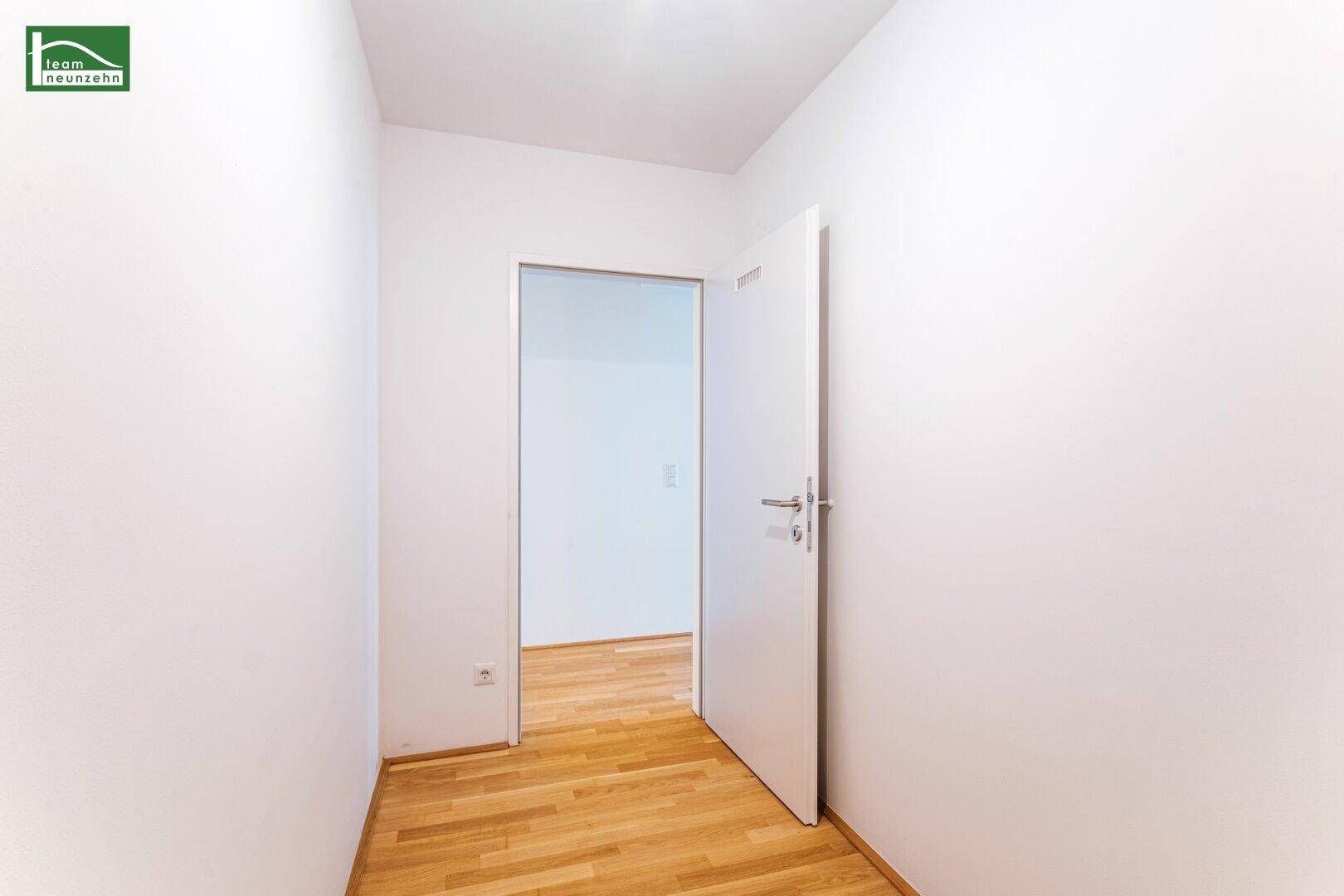 Heller Flur mit Holzboden und einer weißen Tür, die zu einem weiteren Zimmer führt.