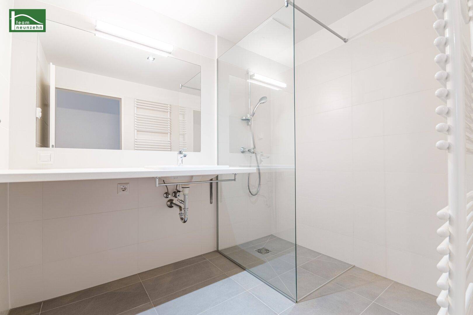 Modernes Badezimmer mit ebenerdiger Glasdusche, großem Waschtisch und beheiztem Handtuchhalter.