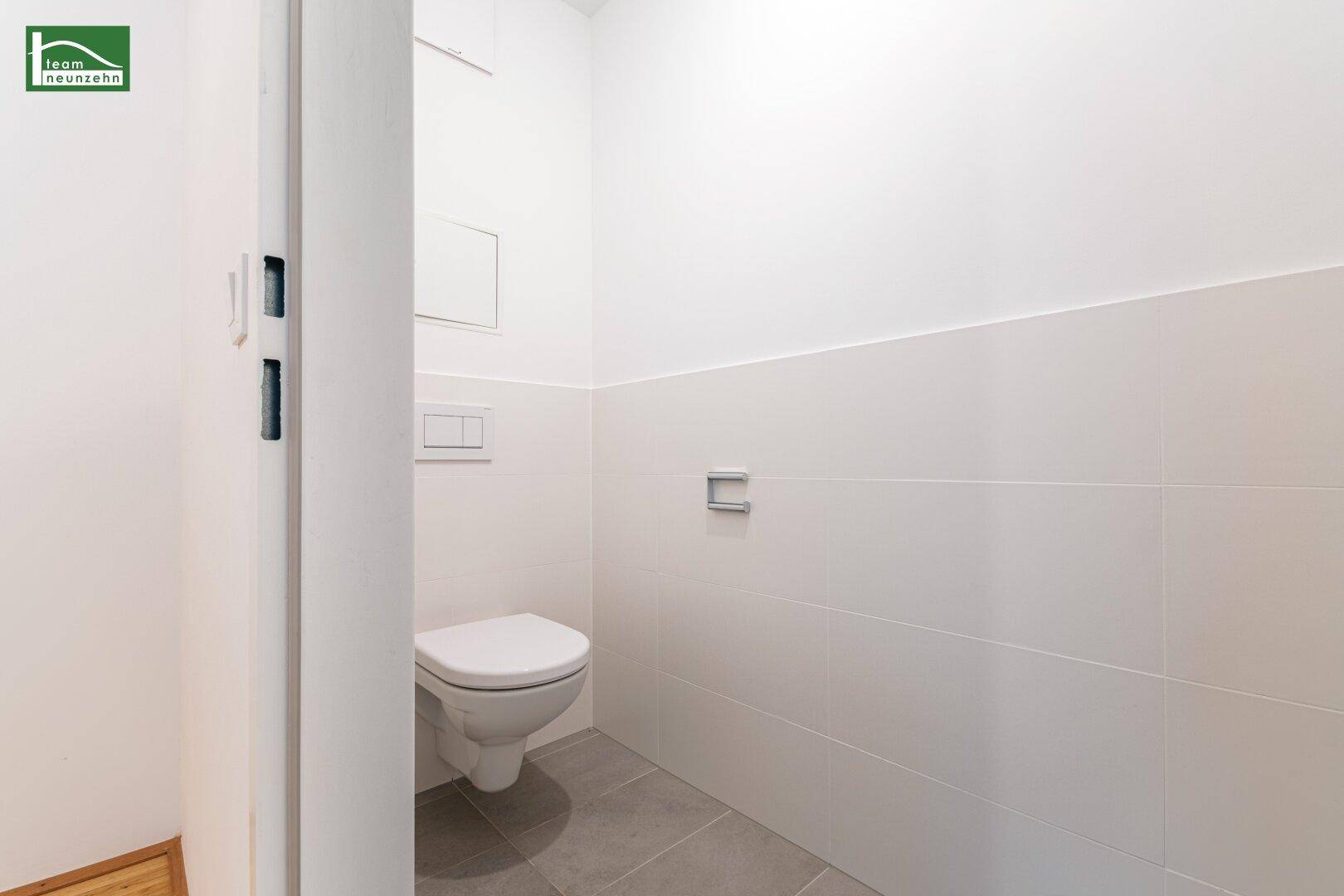 Separates Gäste-WC mit wandhängender Toilette und modernen, hellen Fliesen.