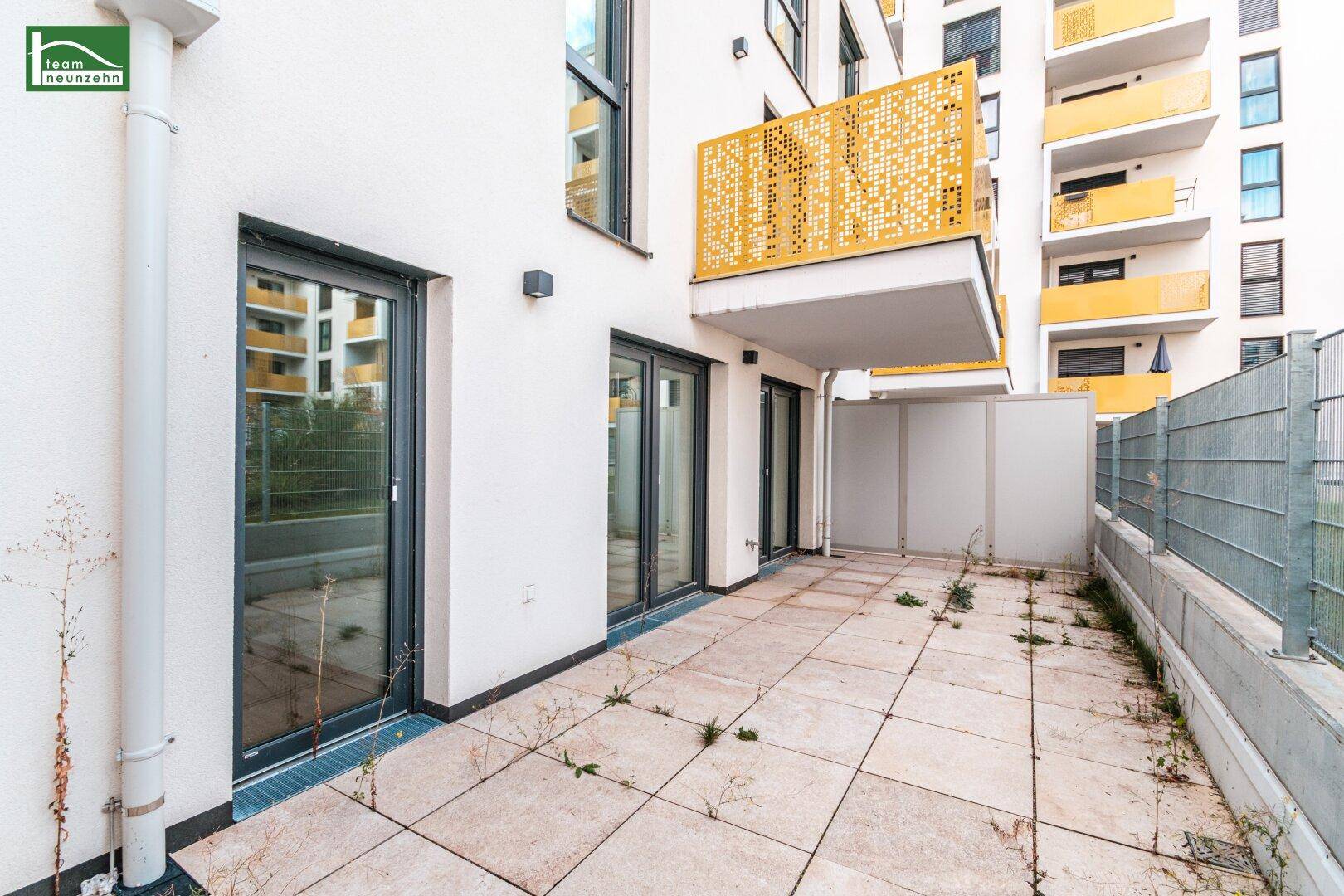 Blick auf die gepflasterte Terrasse mit Zugang zu den Innenräumen und einem Balkon darüber.