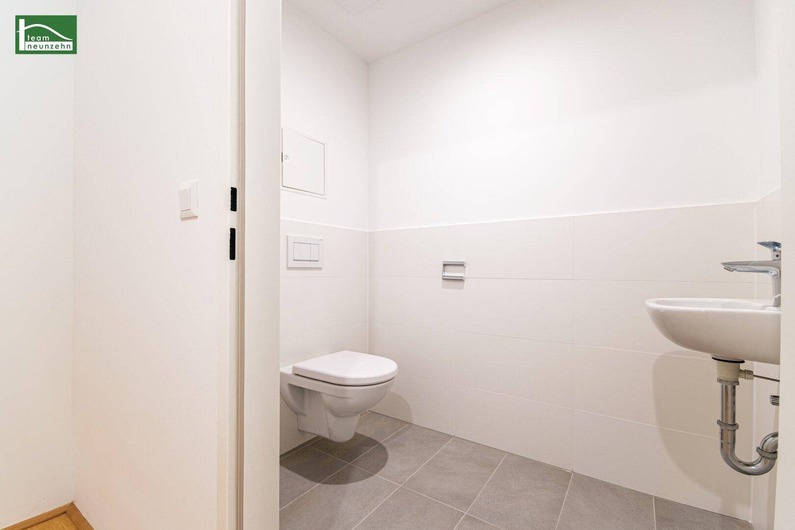 Modernes Gäste-WC mit Wand-WC, Waschbecken und Fliesenboden.