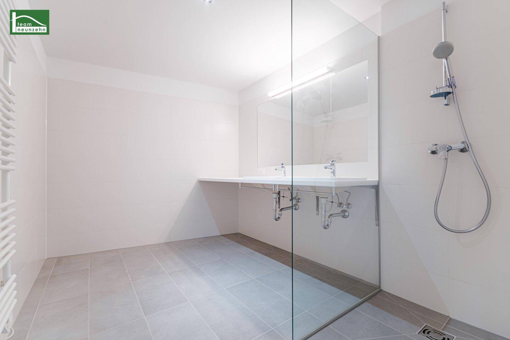 Modernes Badezimmer mit Doppelwaschbecken, großer Dusche und beheiztem Handtuchhalter.