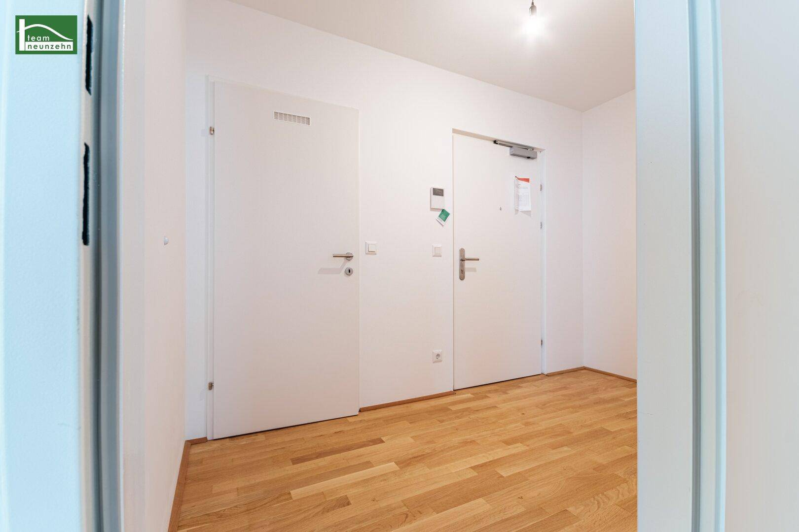 Heller Flur mit Holzboden und zwei Türen, die zu verschiedenen Räumen führen.