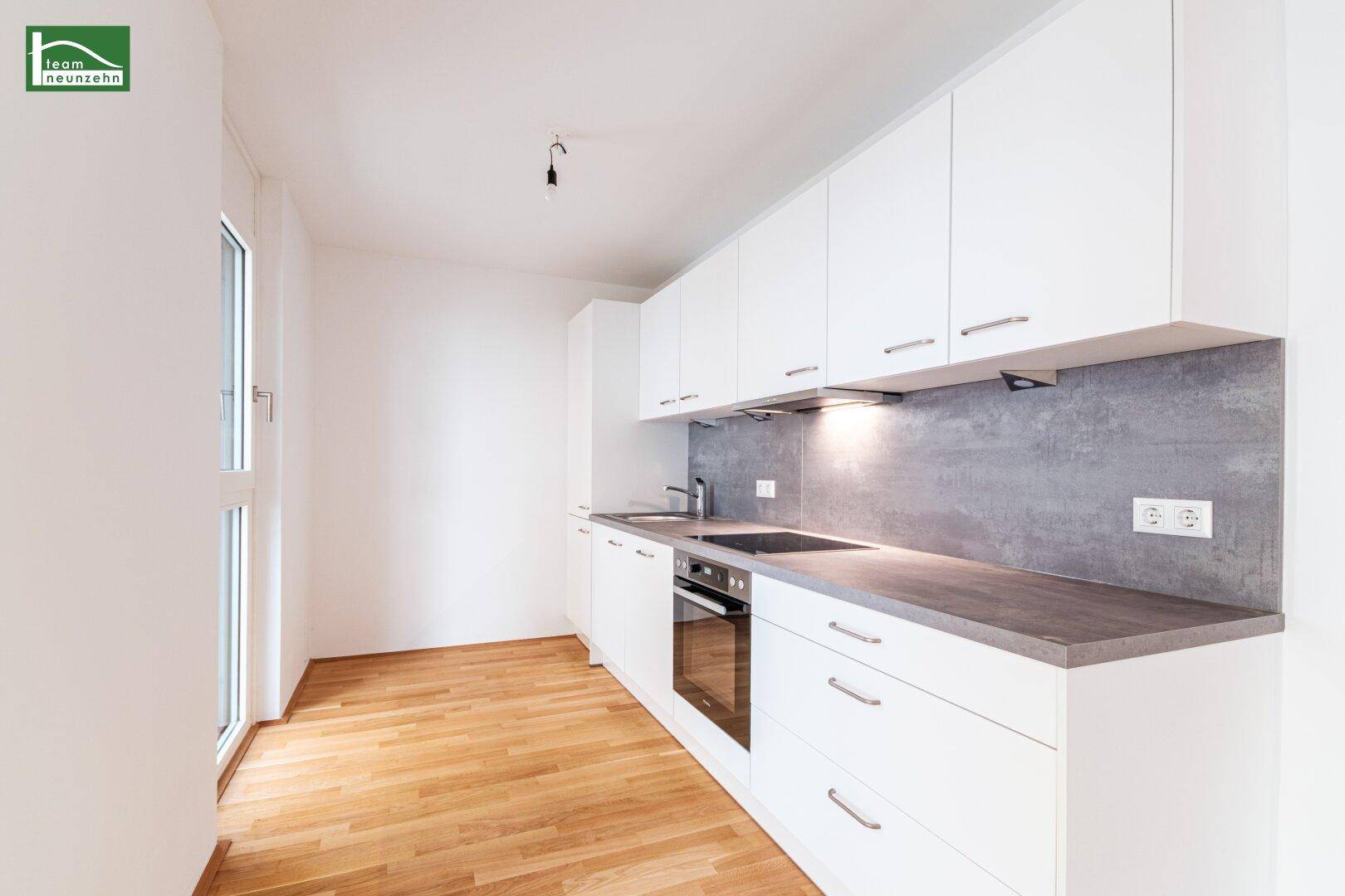 Moderne Einbauküche mit weißen Schränken, dunkler Arbeitsplatte und Holzboden.