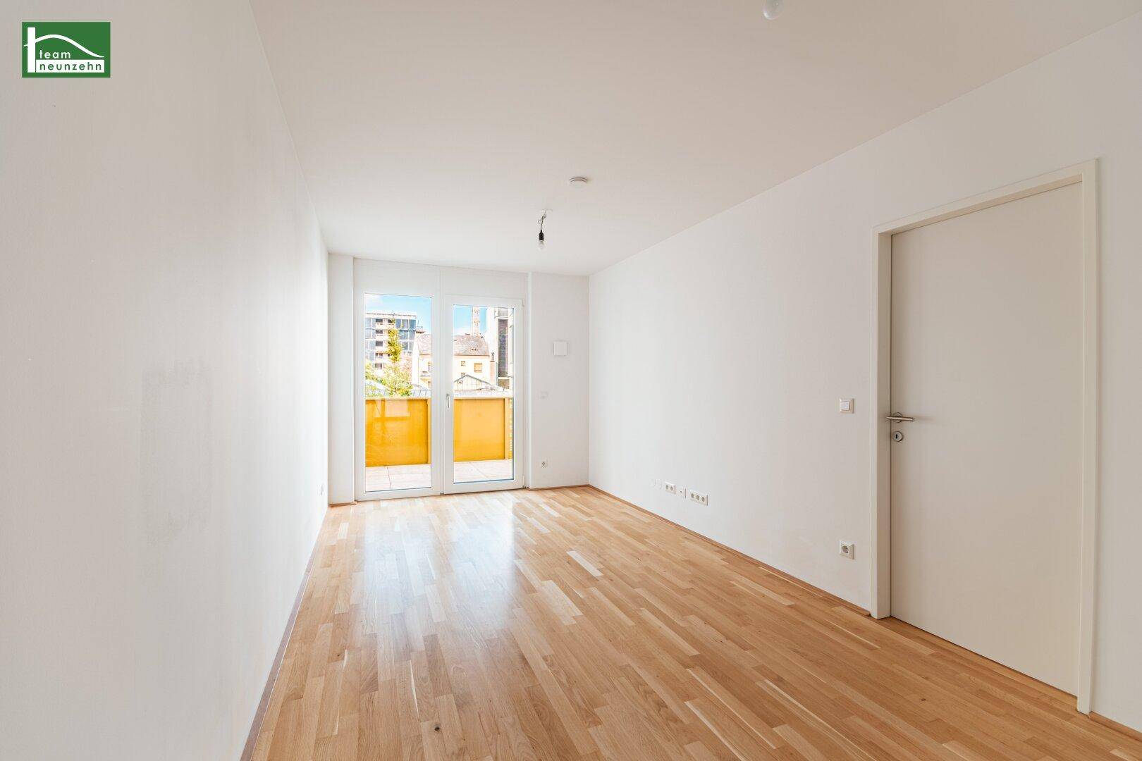 Helles Zimmer mit Parkettboden und Zugang zu einem Balkon mit Stadtblick.