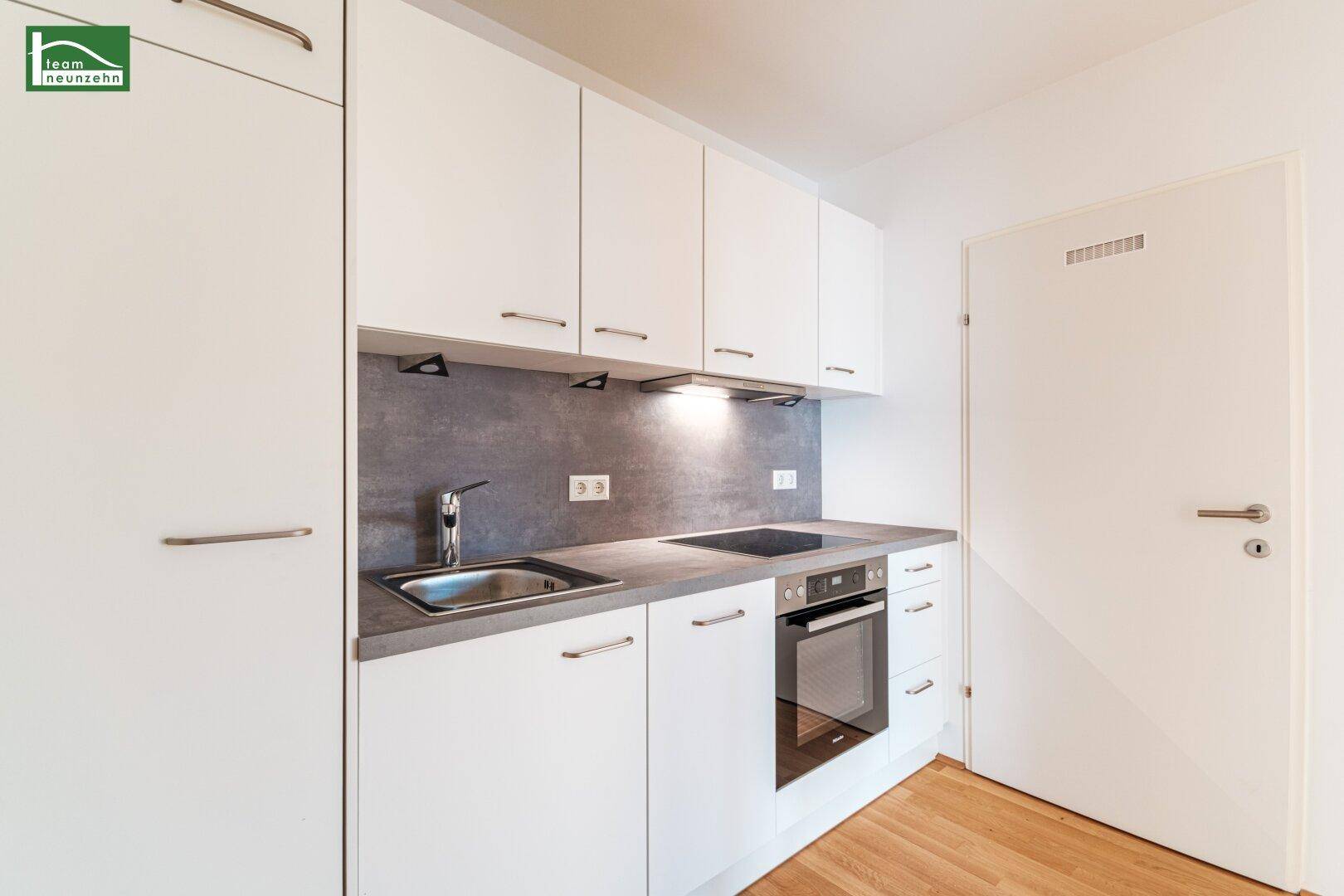 Moderne Küchenzeile mit weißen Schränken, integriertem Backofen und Induktionskochfeld.