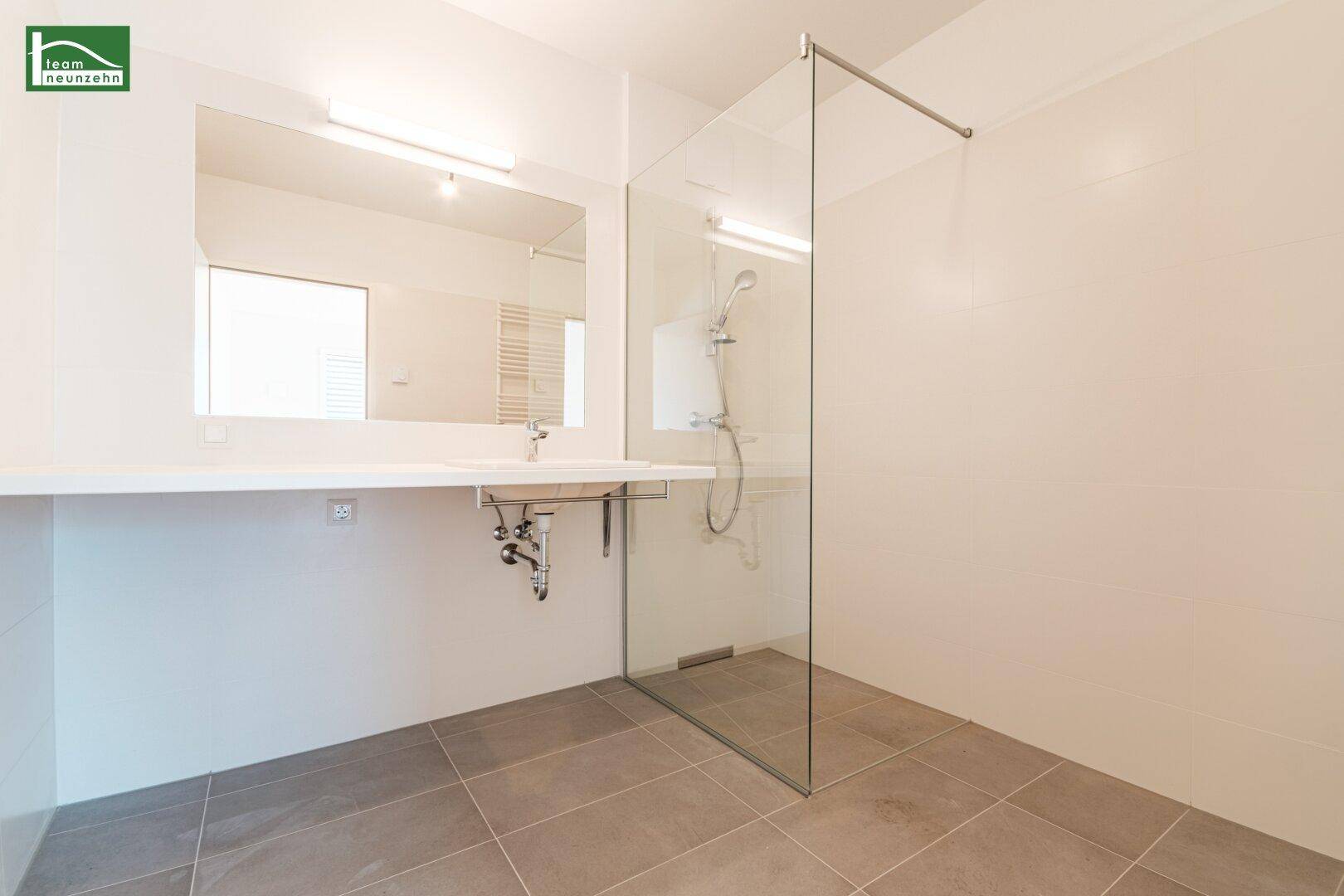 Modernes Badezimmer mit ebenerdiger Dusche, großem Spiegel und Einzelwaschbecken.