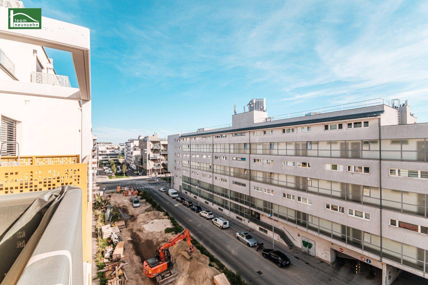Weitblick von einem Balkon über eine städtische Straße mit Gebäuden und einer Baustelle.