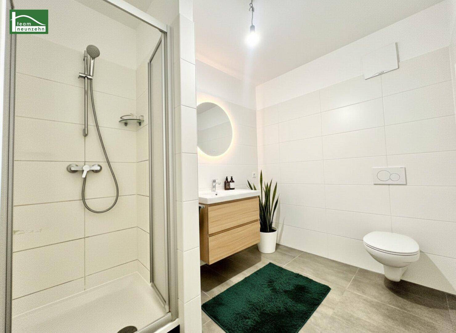 Stilvolles Badezimmer mit Dusche, modernem Waschtisch und beleuchtetem Spiegel.
