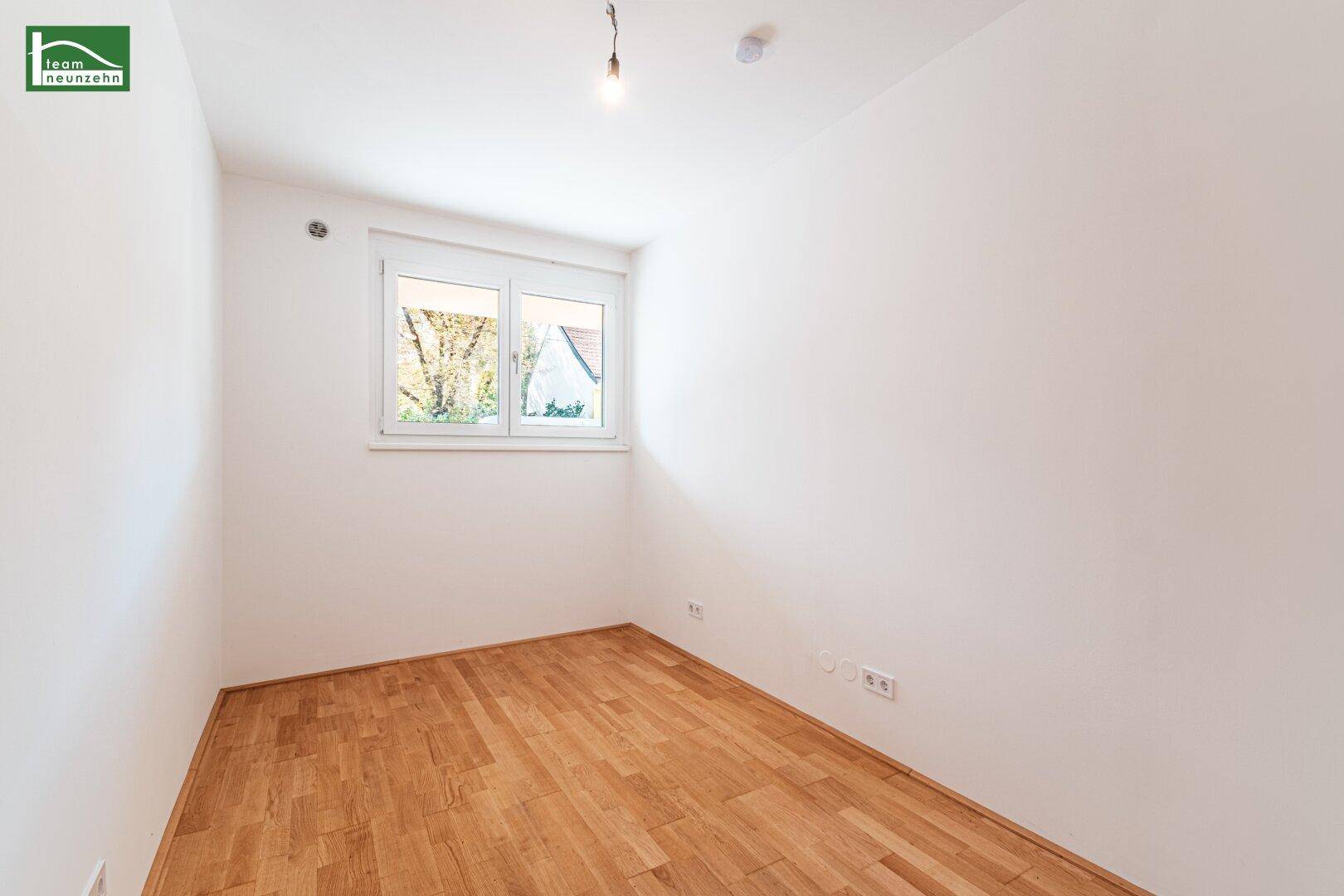 Helles, leeres Zimmer mit Parkettboden und Fenster, geeignet als Kinder- oder Gästezimmer.