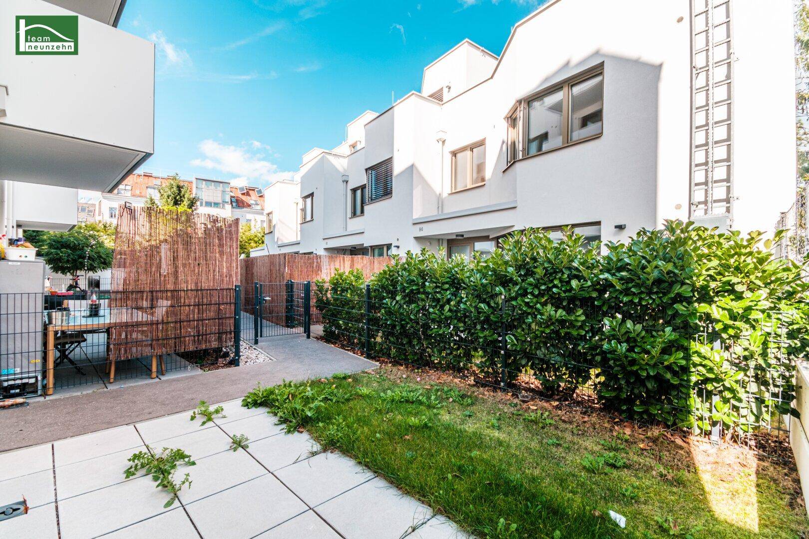 Kleiner privater Gartenbereich mit Terrasse und Hecke vor modernen Reihenhäusern.