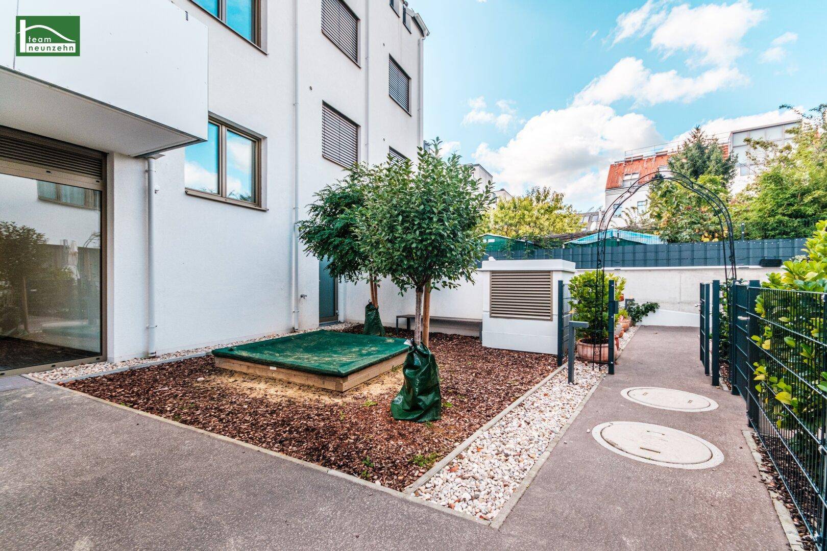 Kleiner Spielbereich mit Sandkasten und Bäumen in einem Gemeinschaftsgarten.