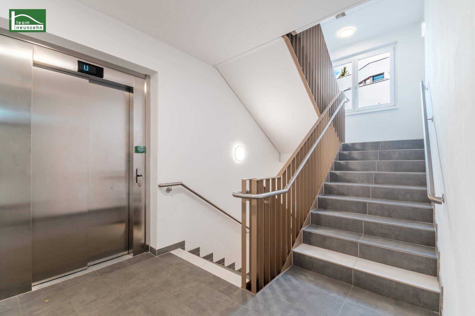 Heller Treppenaufgang mit modernem Geländer und einem Aufzug in einem Mehrfamilienhaus.