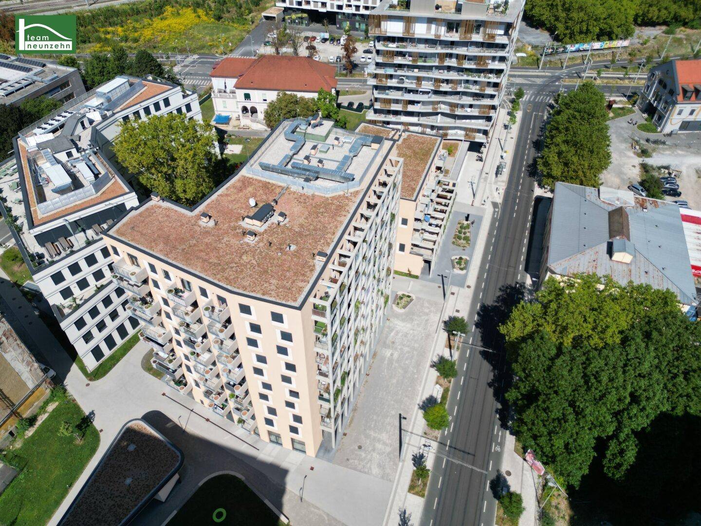 Draufsicht auf einen modernen Gebäudekomplex mit begrünten Flachdächern und Balkonen in städtischer Umgebung.