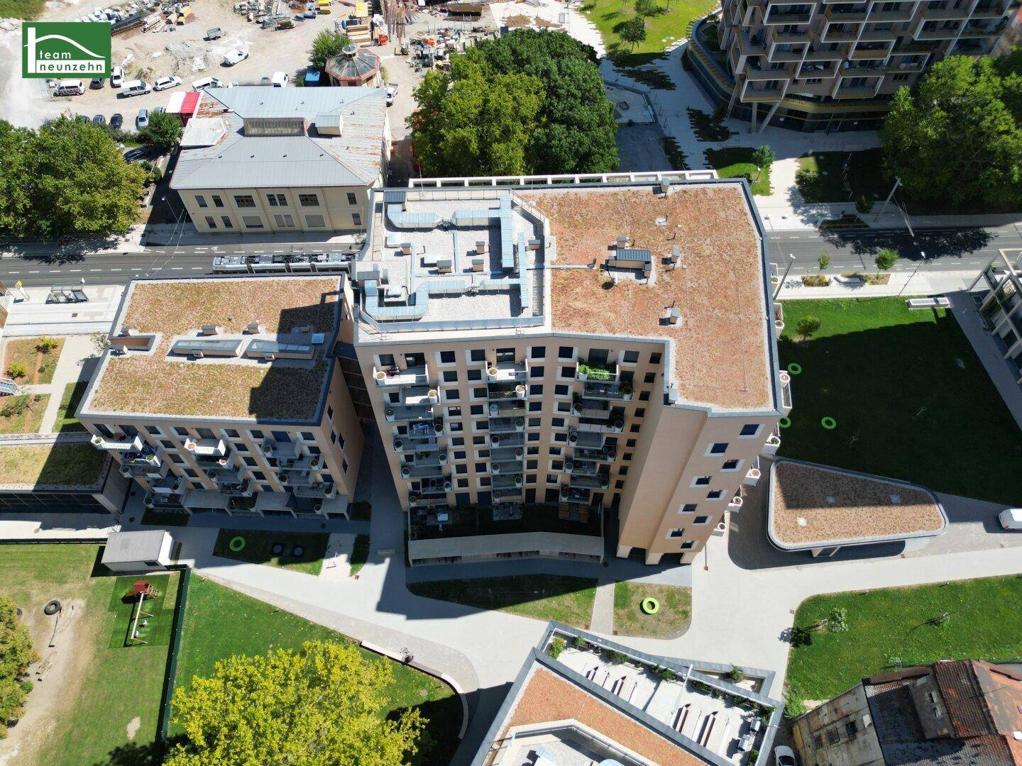 Luftaufnahme eines modernen Wohnkomplexes, umgeben von Grünflächen und Bäumen unter blauem Himmel.