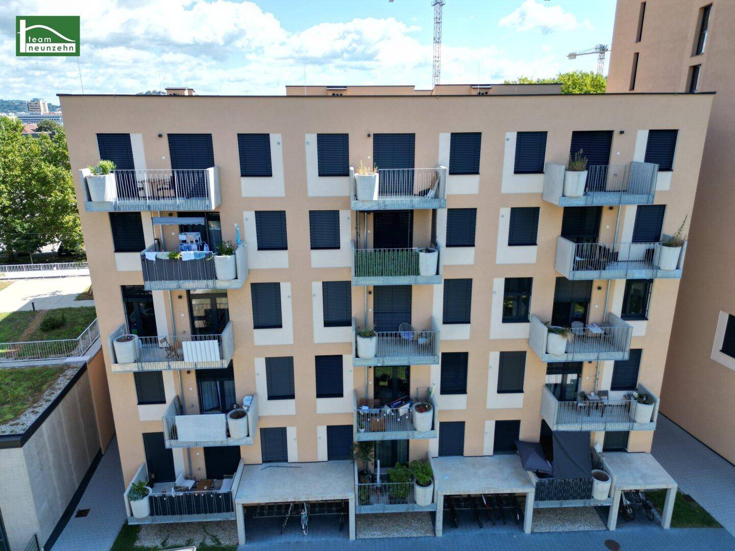 Fassade eines modernen Wohngebäudes mit zahlreichen Balkonen, Fenstern und dunklen Rollläden.