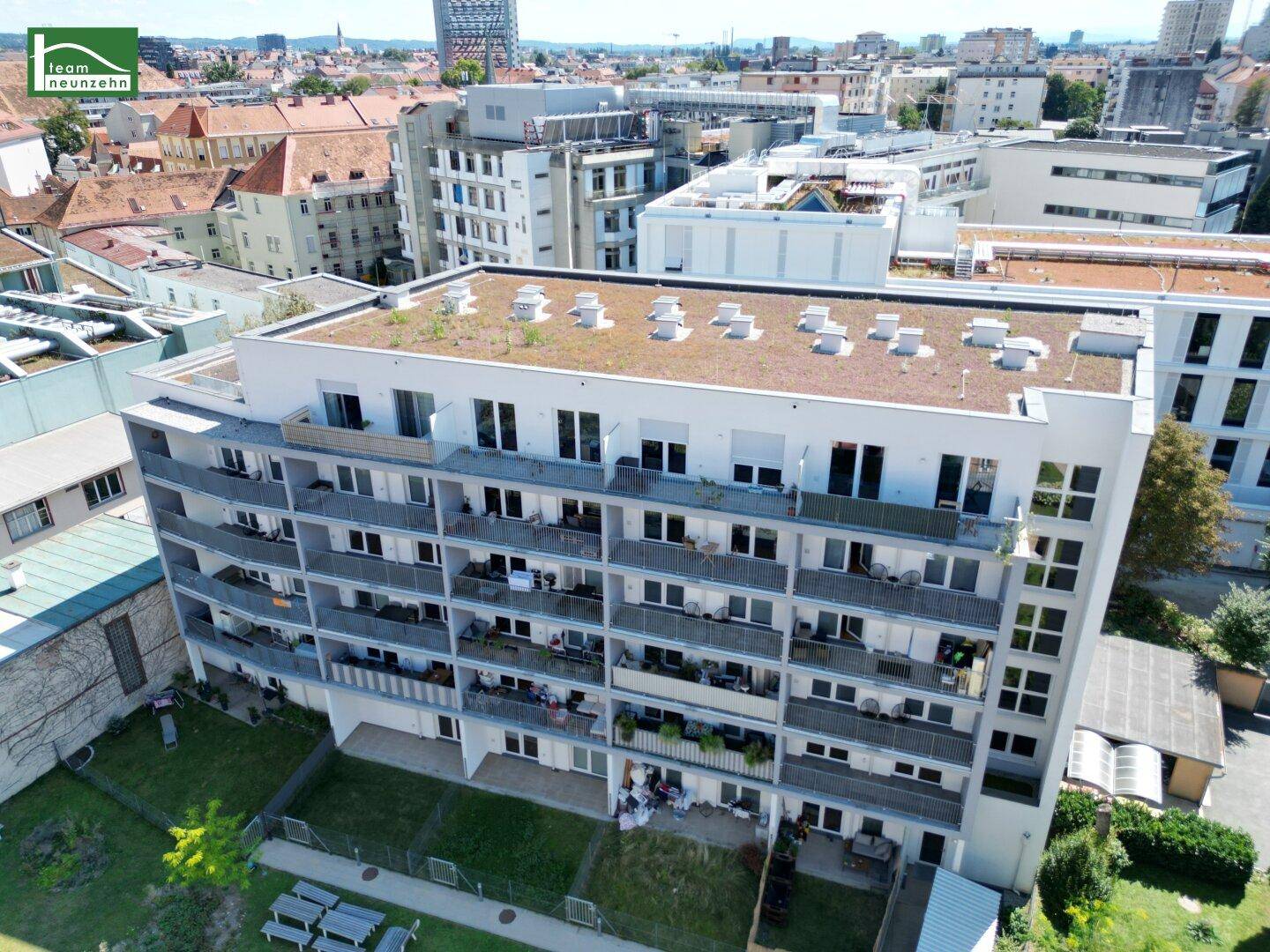 Luftaufnahme eines modernen Wohngebäudes mit begrüntem Flachdach und zahlreichen Balkonen in städtischer Umgebung.