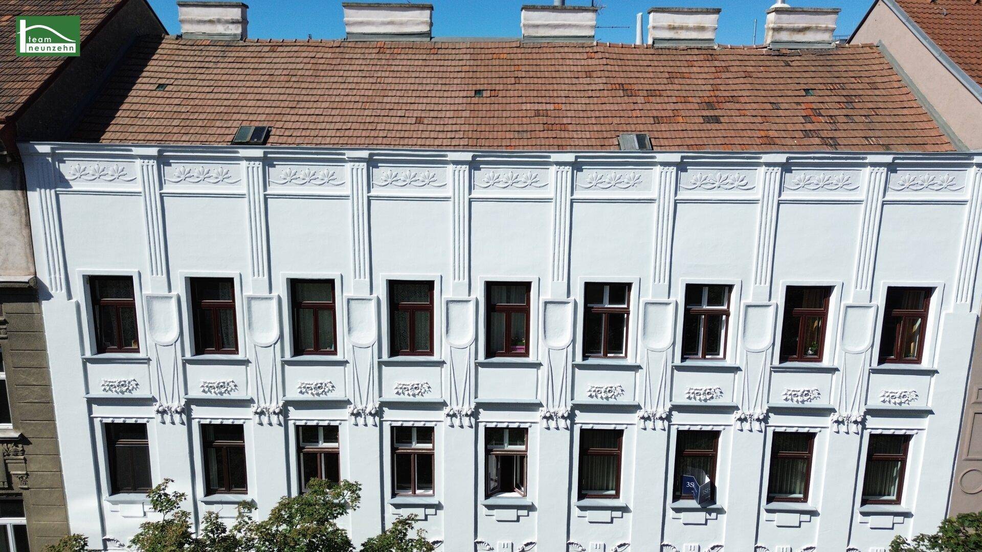 Detaillierte Luftaufnahme der frisch renovierten Fassade mit vielen Fenstern und Ziegeldach.