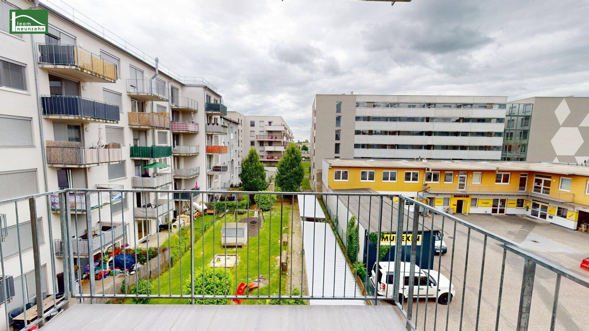 Blick vom Balkon auf einen grünen Innenhof mit Spielplatz und umliegenden Gebäuden.