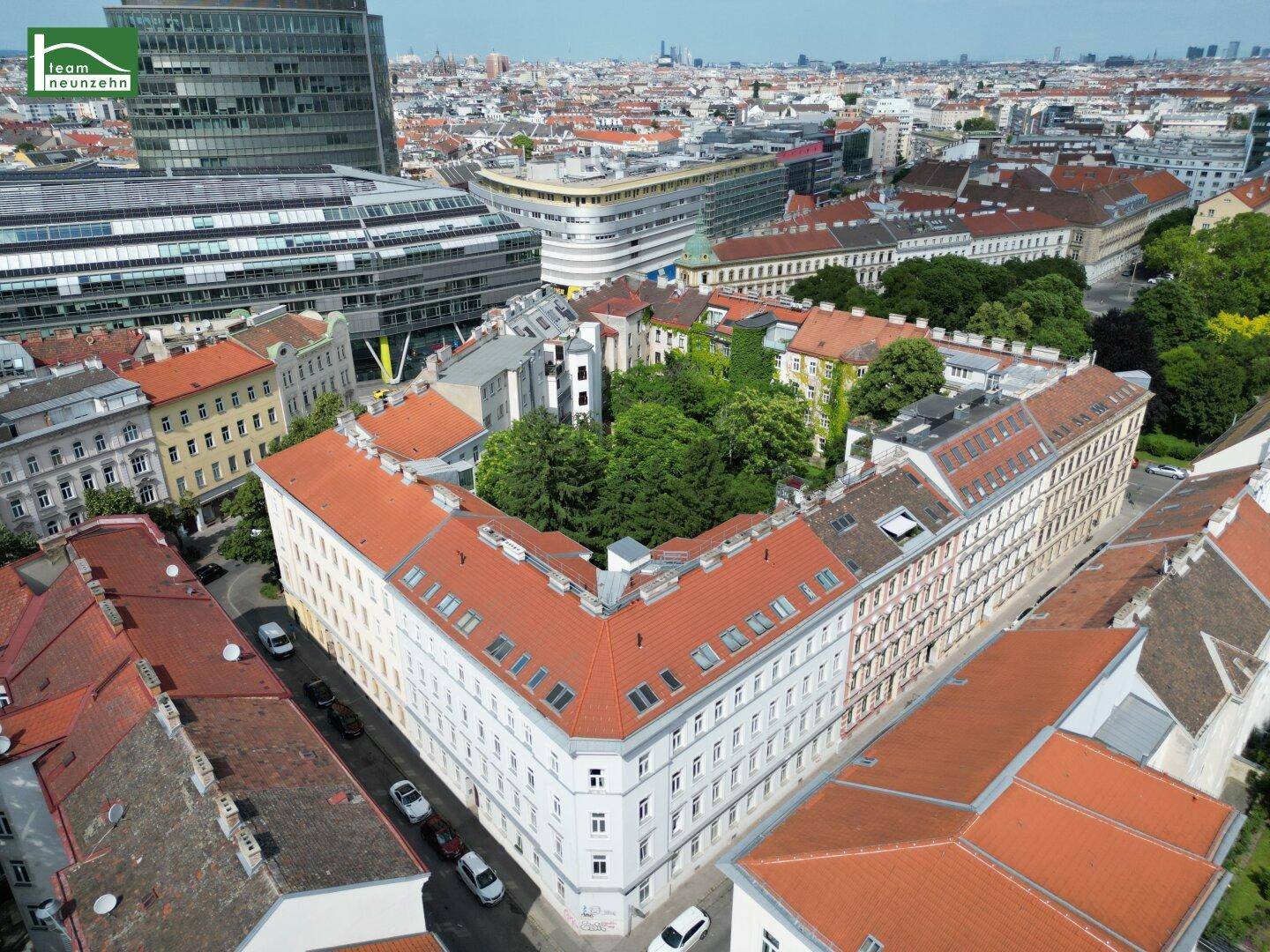 Weitläufige Luftaufnahme eines Stadtblocks mit einem großen Gebäude, umgeben von viel Grün und städtischer Bebauung.