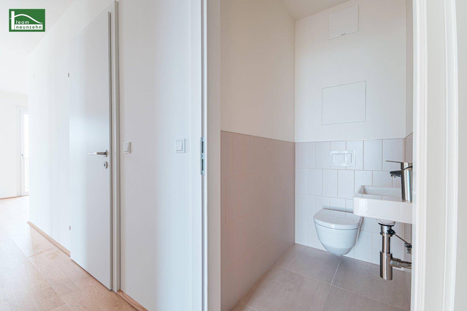 Separates Gäste-WC mit wandhängender Toilette, Waschbecken und Fliesenboden.