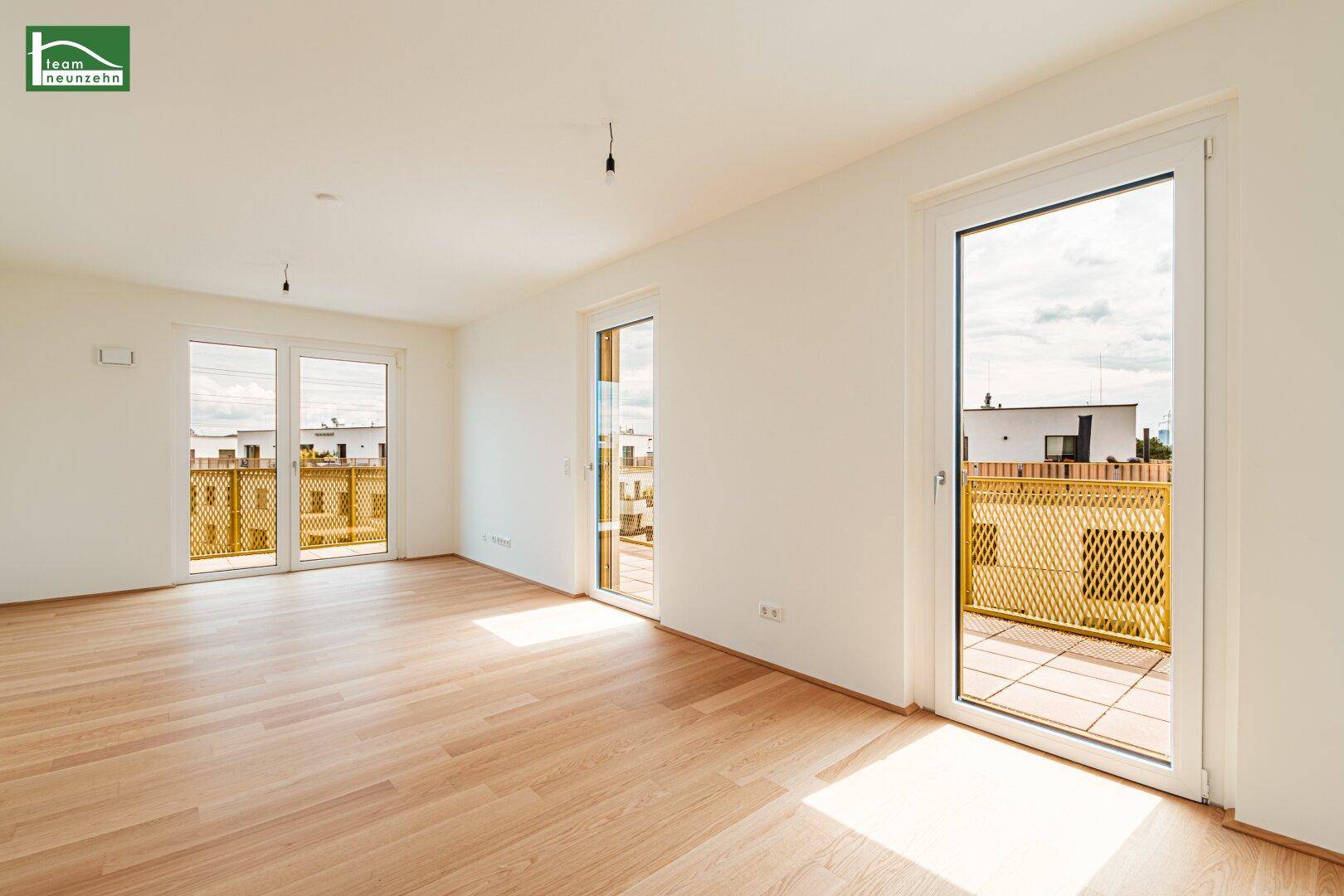 Geräumiges Wohnzimmer mit Holzboden und mehreren Zugängen zu einem langen Balkon.