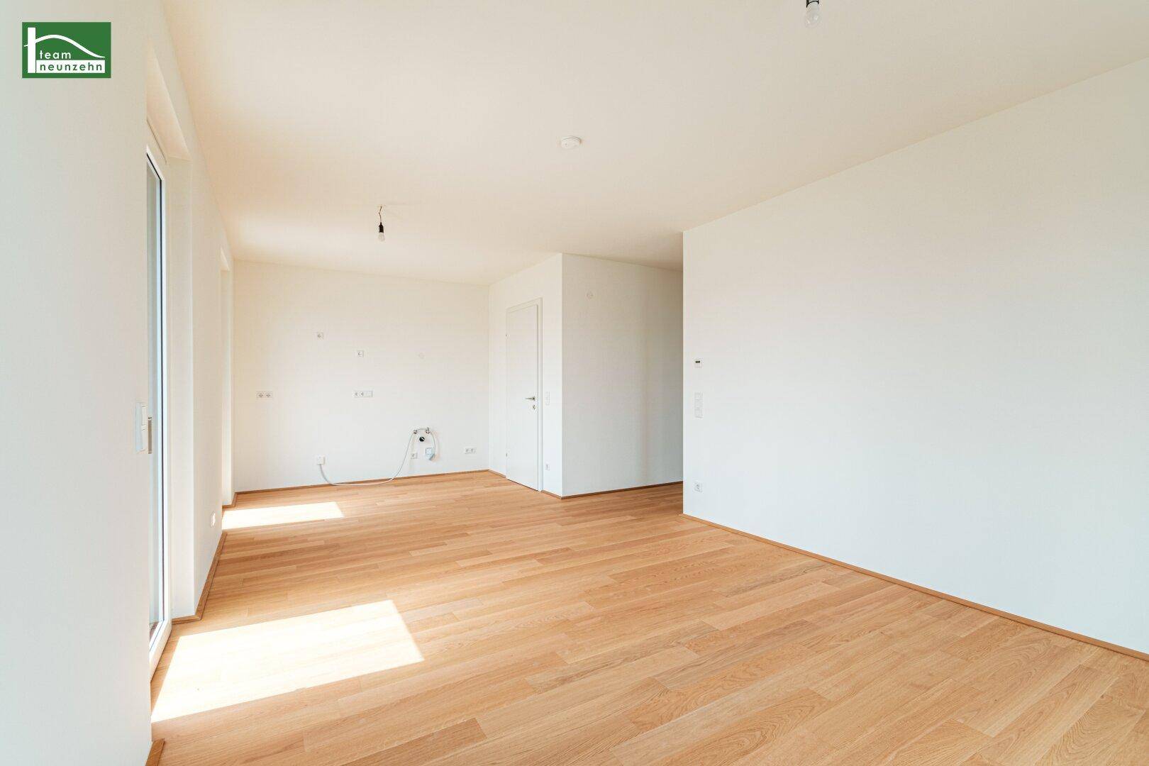 Helles, leeres Wohnzimmer mit Holzboden und Zugang zu einem Balkon.