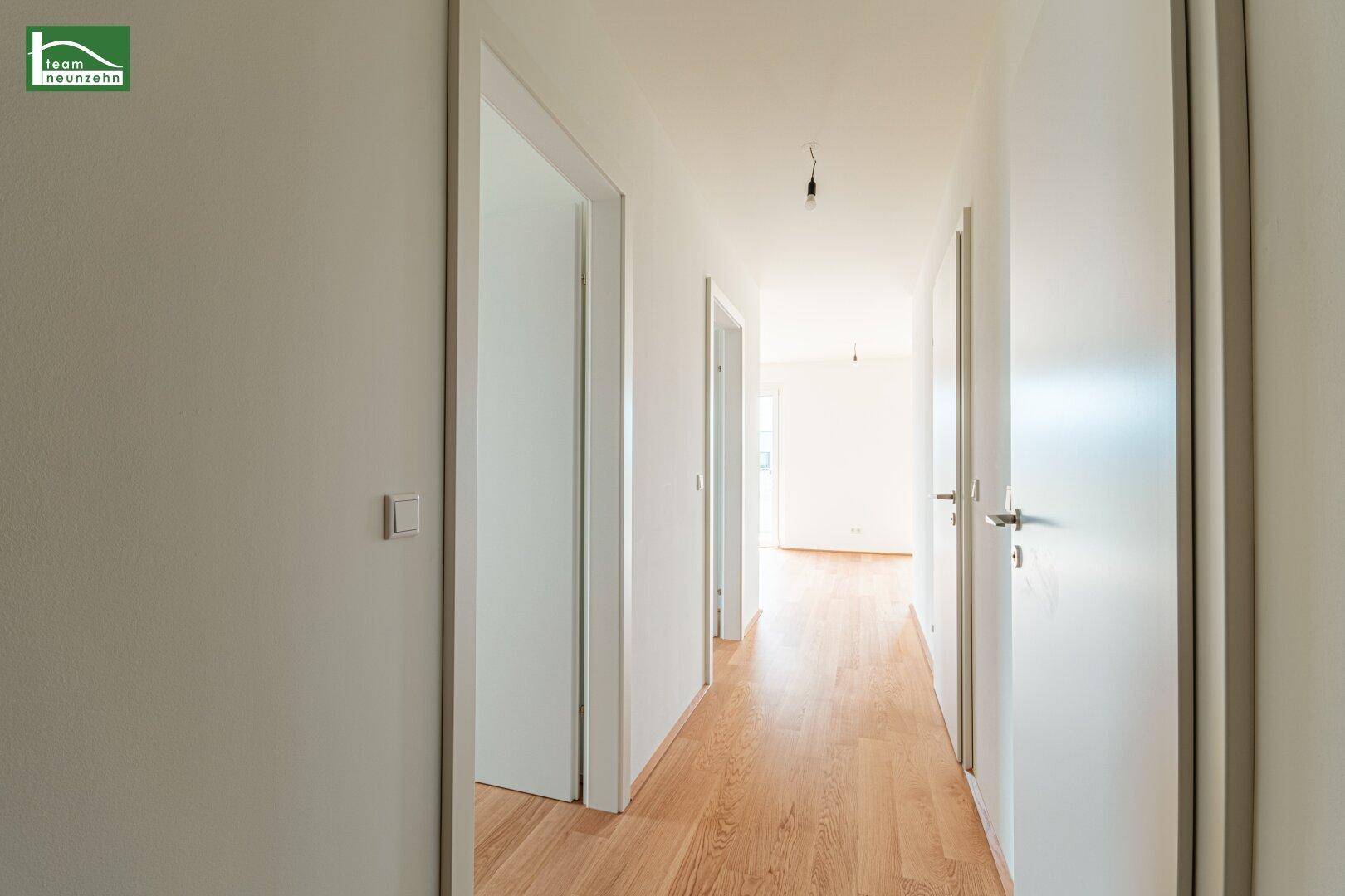 Heller Flur mit Holzboden und weißen Türen, der zu weiteren Räumen führt.