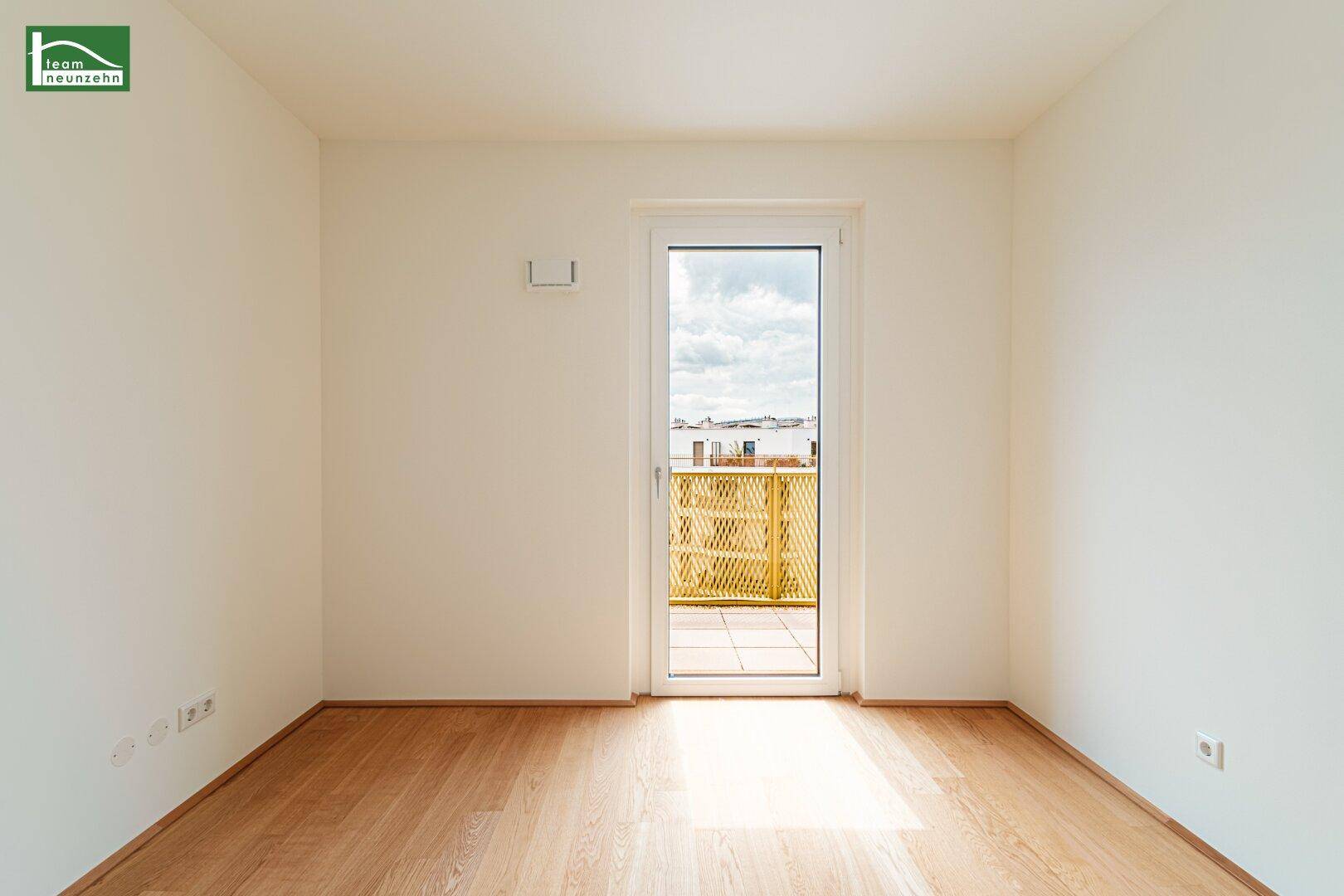 Heller, leerer Raum mit Holzboden und Zugang zu einem Balkon oder einer Terrasse.