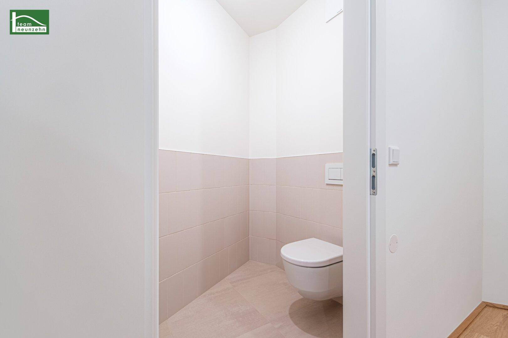 Separate Gästetoilette mit wandmontiertem WC und hellen Fliesen an den Wänden.