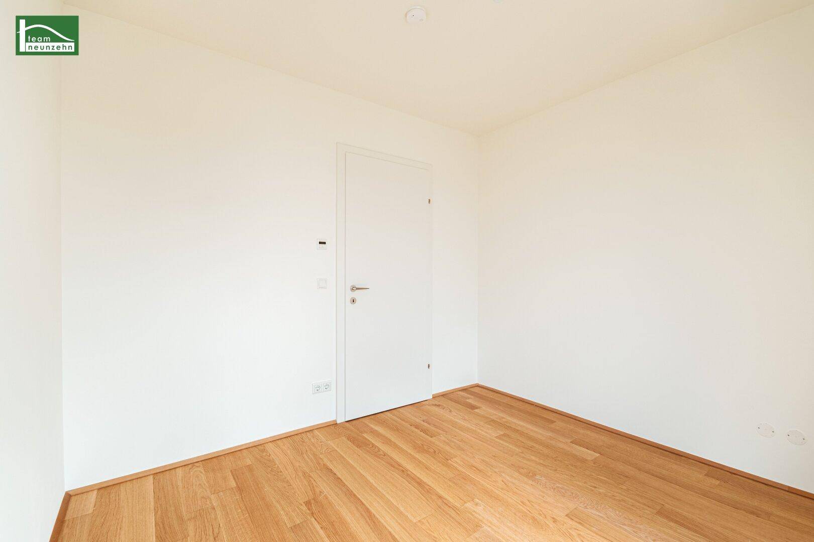 Leeres Zimmer mit Holzboden und weißer Tür, bietet vielseitige Nutzungsmöglichkeiten.