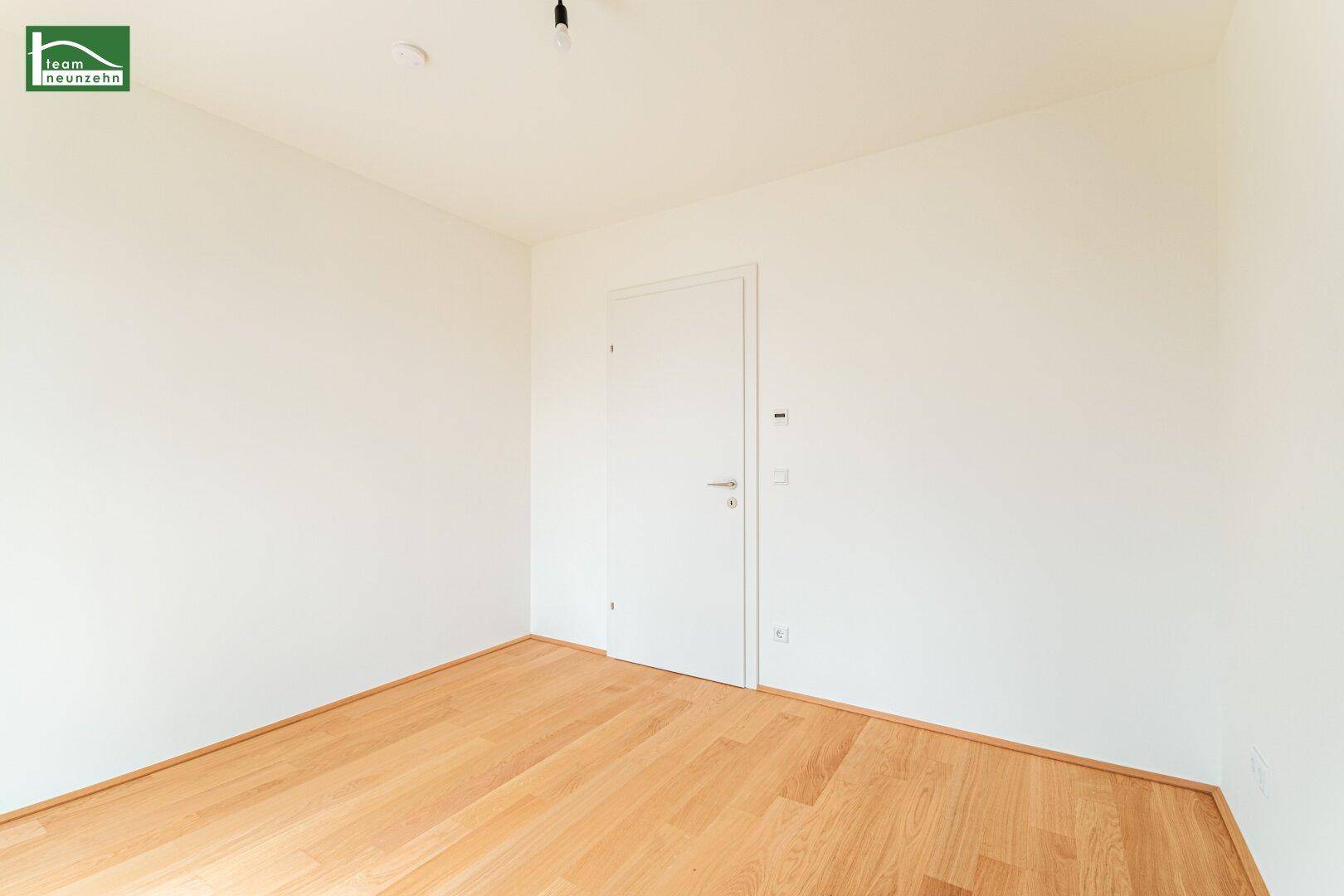 Leeres Zimmer mit Holzboden und weißer Tür, bereit für die individuelle Einrichtung.