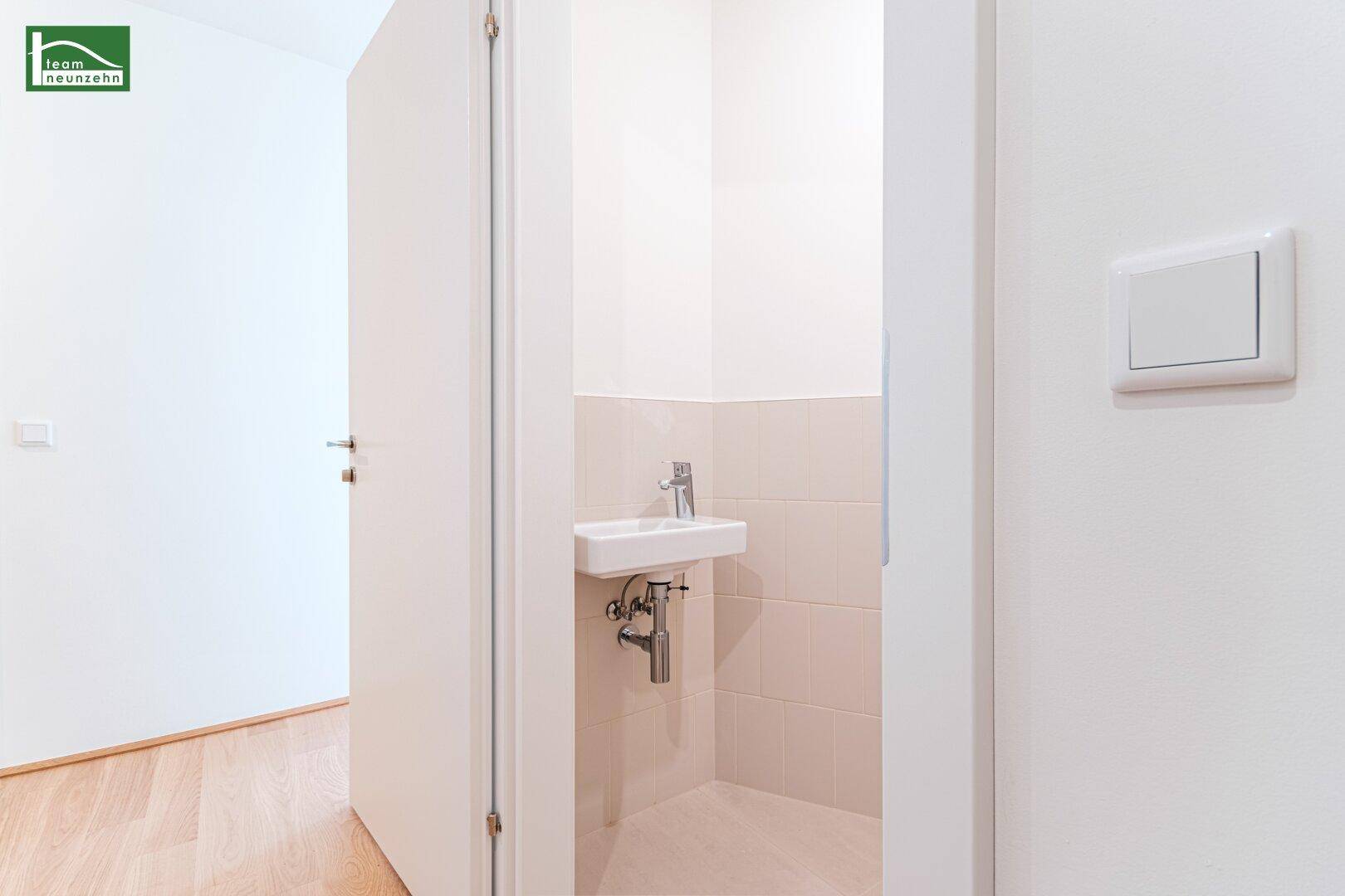 Kleines Gäste-WC mit Wandwaschbecken und hellbeigen Fliesen, praktisch und funktional.