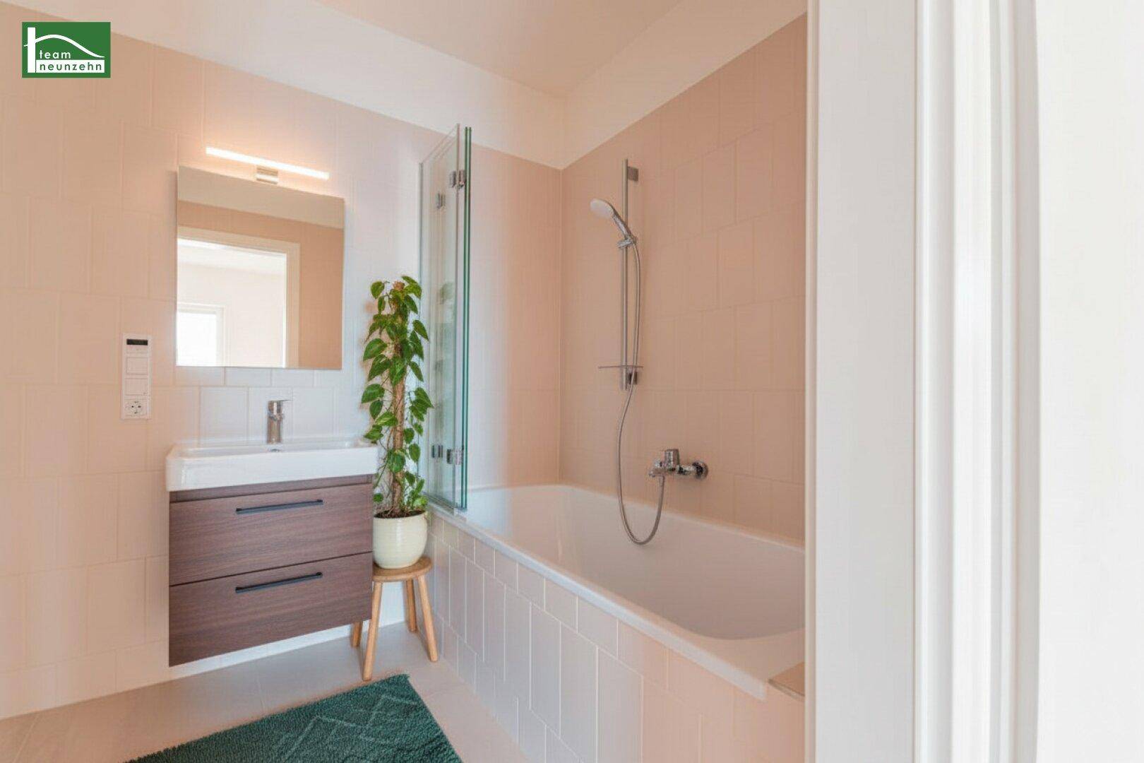 Badezimmer mit Badewanne, Waschtischunterschrank und Spiegel, dekoriert mit einer Pflanze.